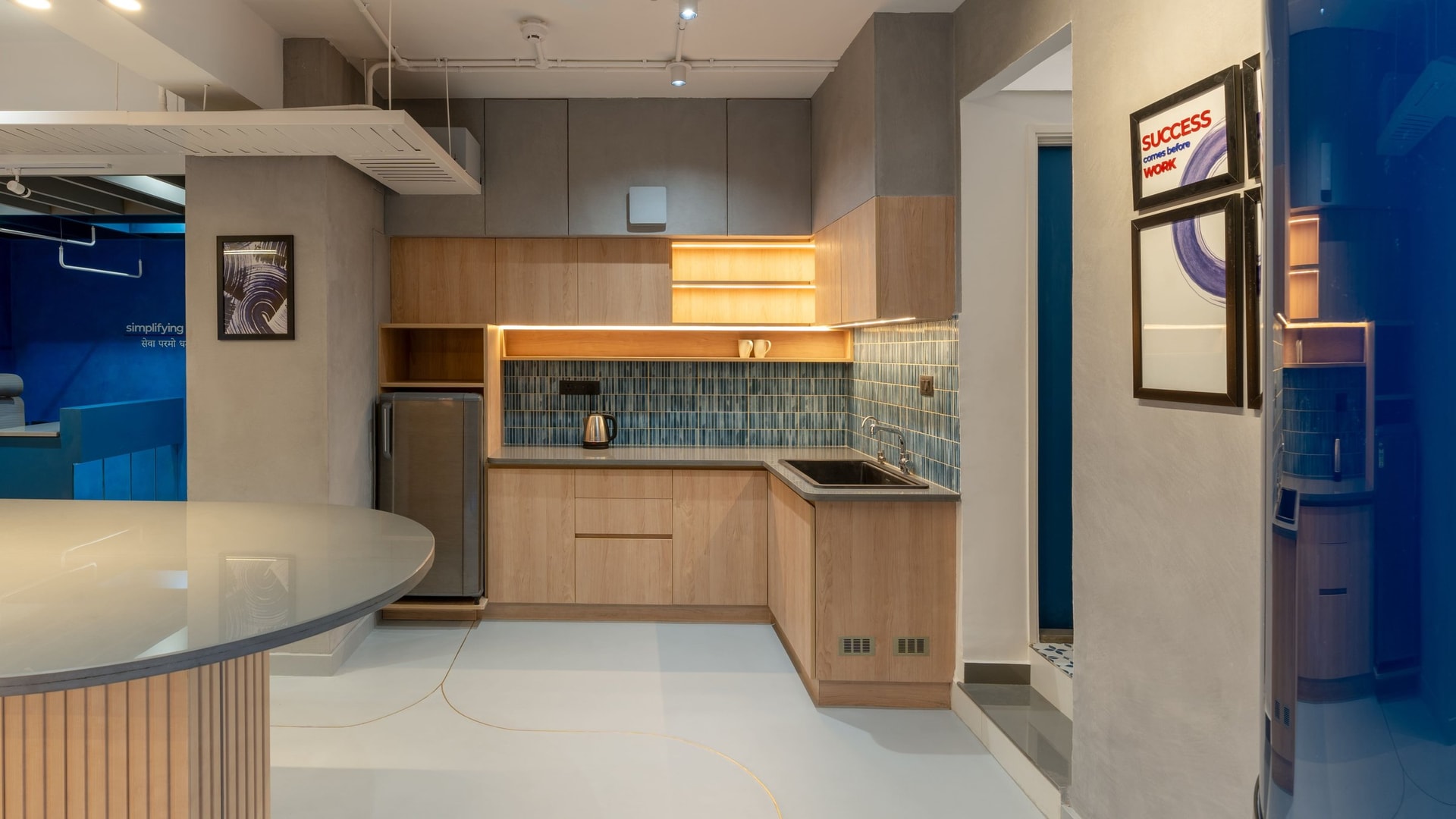 The pantry: hand-glazed tile in graduated blues above light-wood cabinetry, the warmest corner of the office