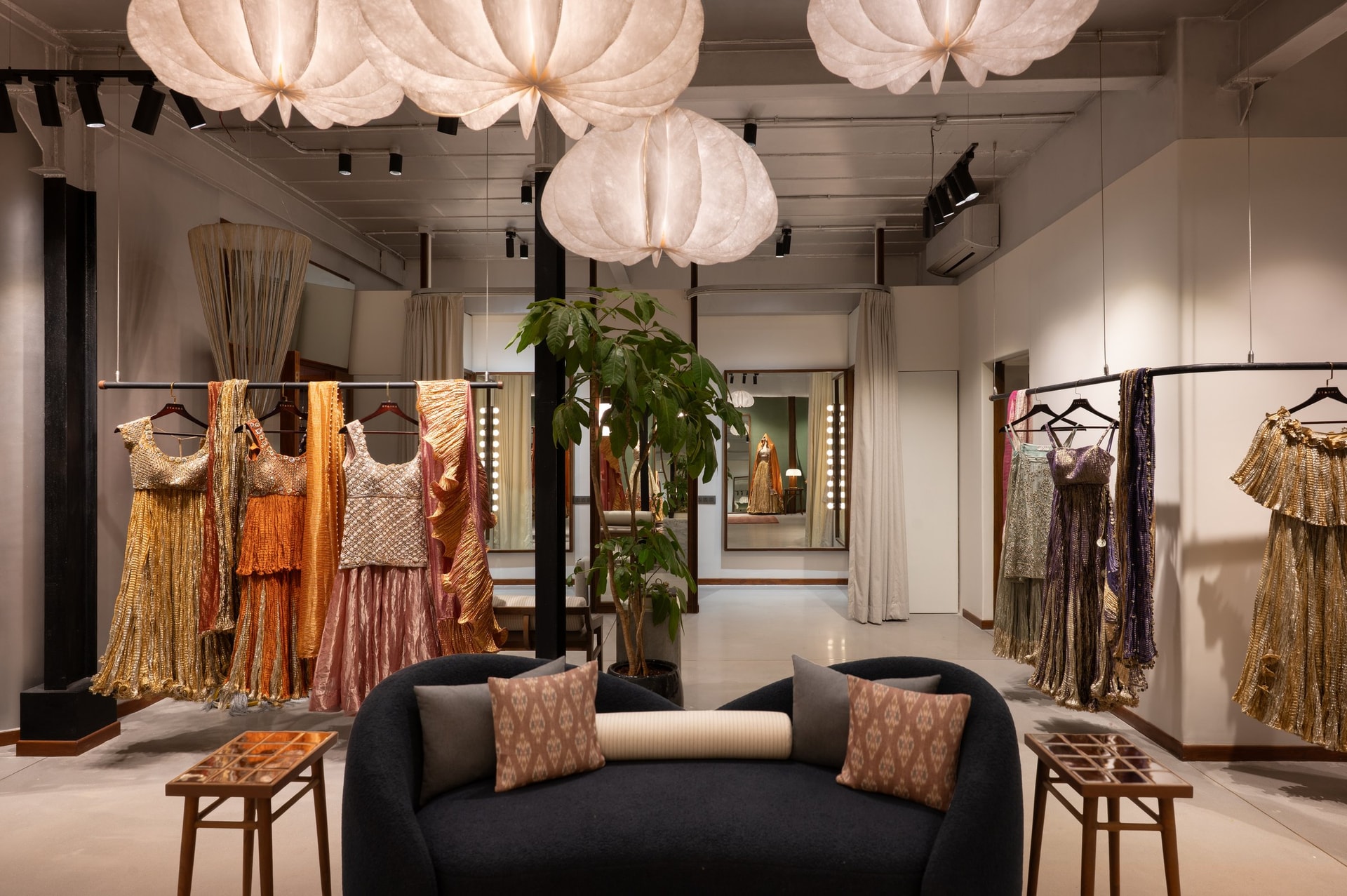 Clustered paper-pleated pendants hang above the central seating, echoing the folded, crinkled register of the garments below