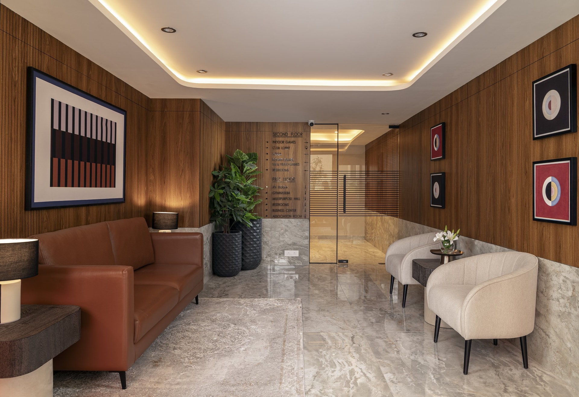 The lower club lobby, panelled in warm wood-grain, where a tan leather sofa anchors the orientation point of the building