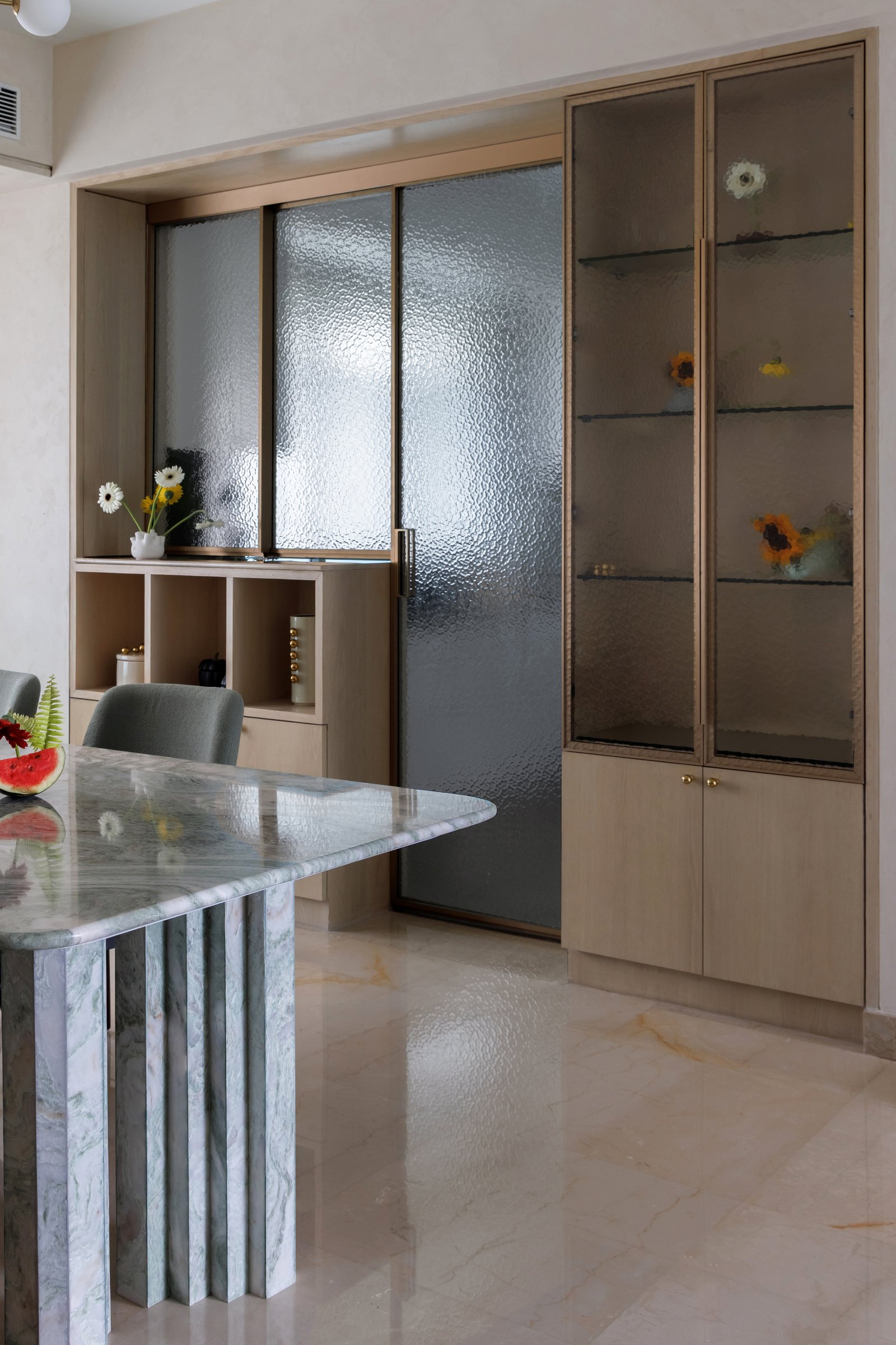 A textured-glass sliding partition leads from the dining area to the kitchen, flanked by a display vitrine and shallow open cubbies