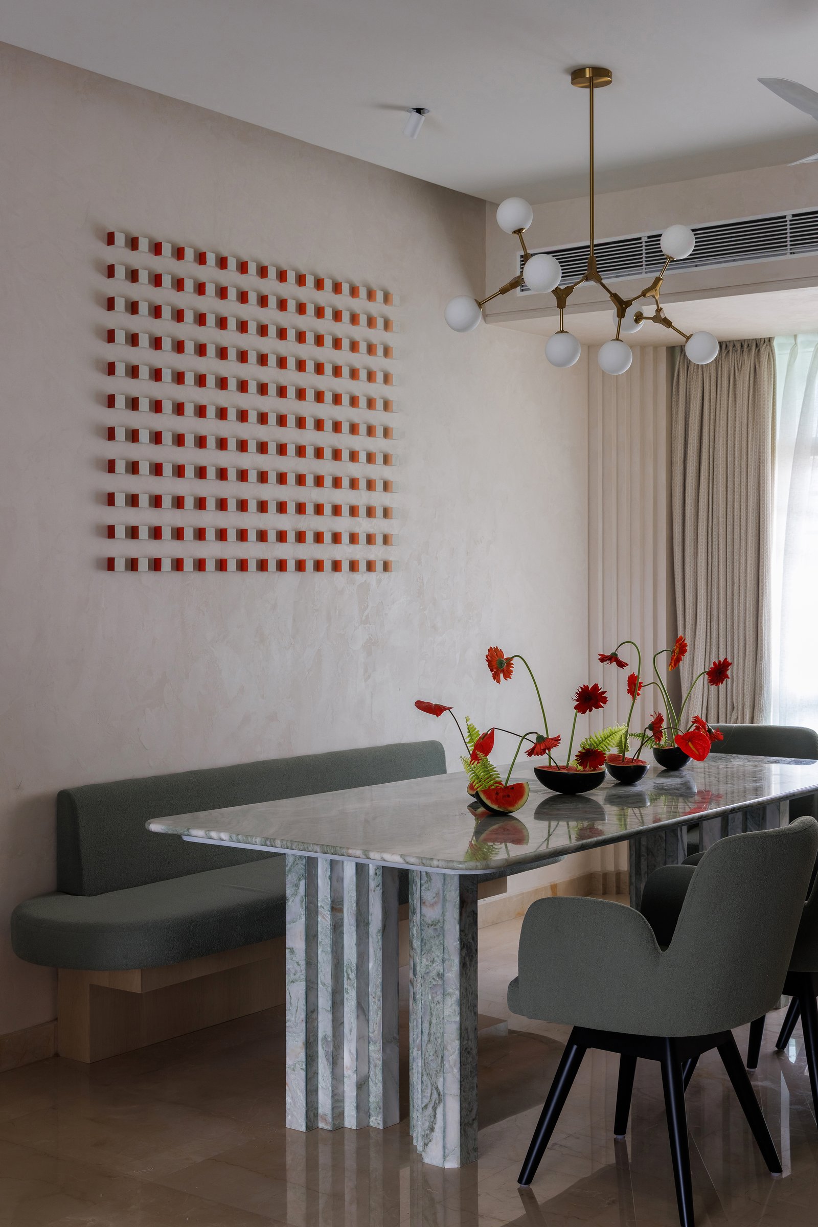 The dining area: a green-veined marble table on a fluted plinth, a sputnik chandelier in brass, and a kinetic coral-and-cream wall work above the built-in bench