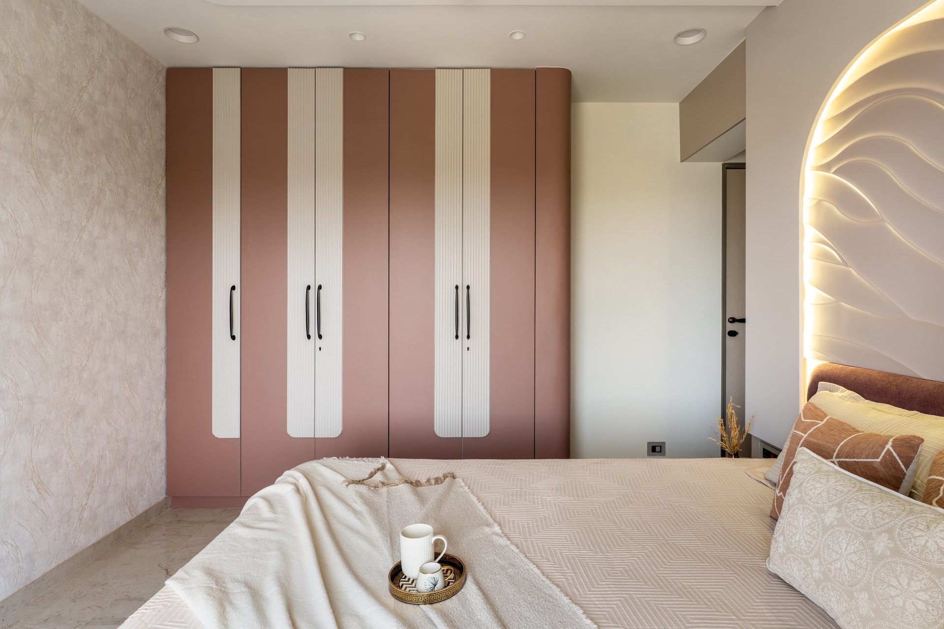 The wardrobe wall in matte terracotta-rose, interrupted by slim fluted ivory panels that read as inlaid columns