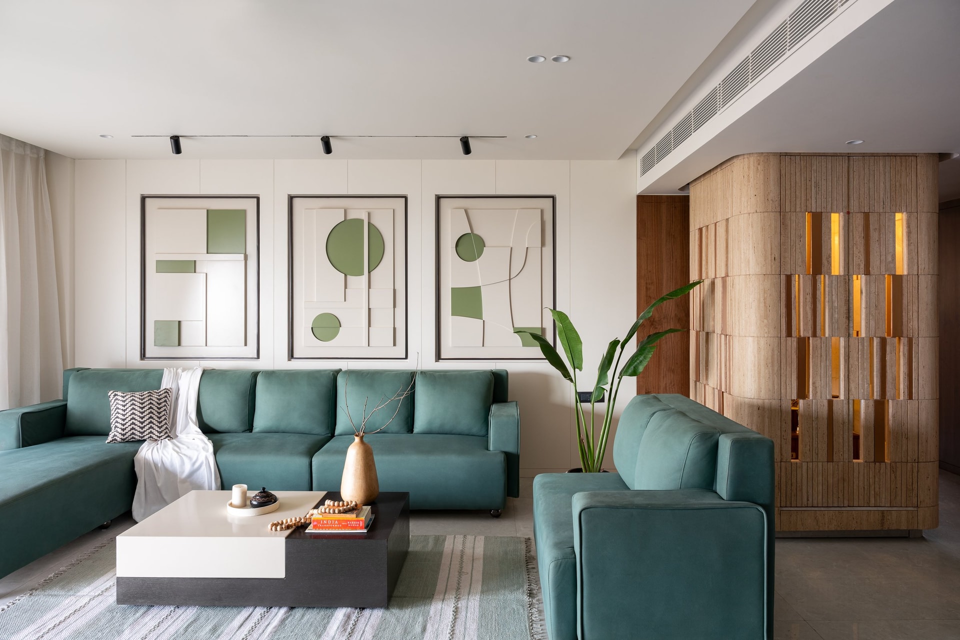 The living room: a triptych of relief artworks in cream and sage anchors the teal sofa, with the temple column glowing at the room's edge