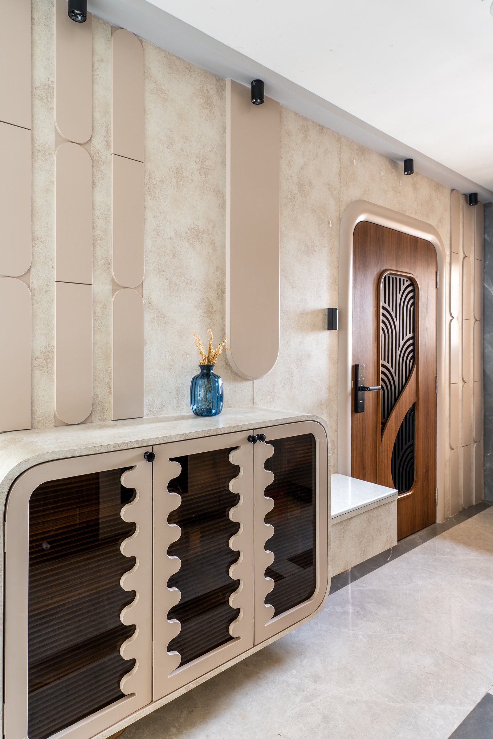 The foyer establishes the home's dune vocabulary: capsule-shaped wall reliefs, a wave-edged console, and an arched timber door cut with curvilinear inserts
