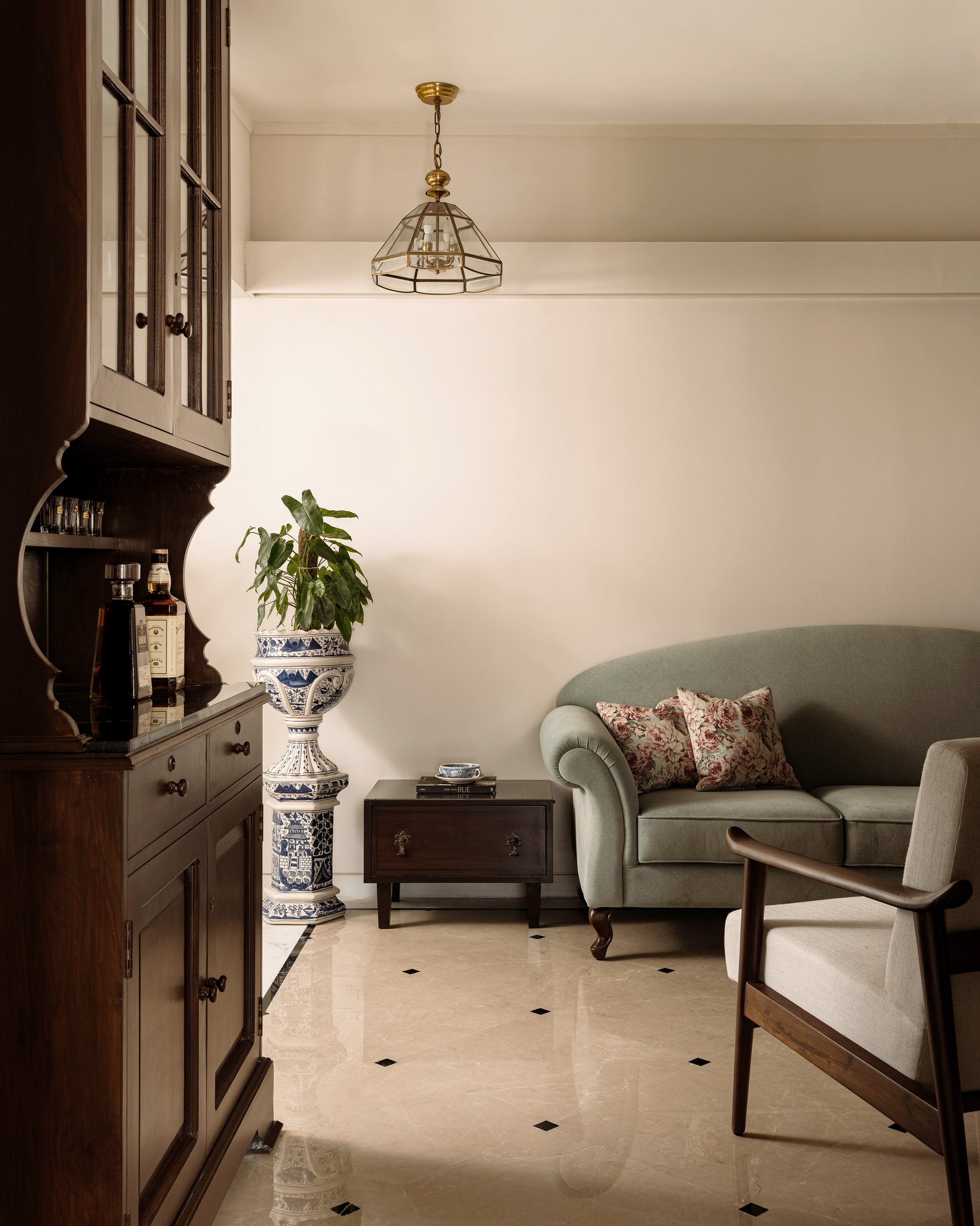 The living room, where an inherited blue-and-white pedestal planter holds its place between a dark wood display cabinet and a curved sage sofa