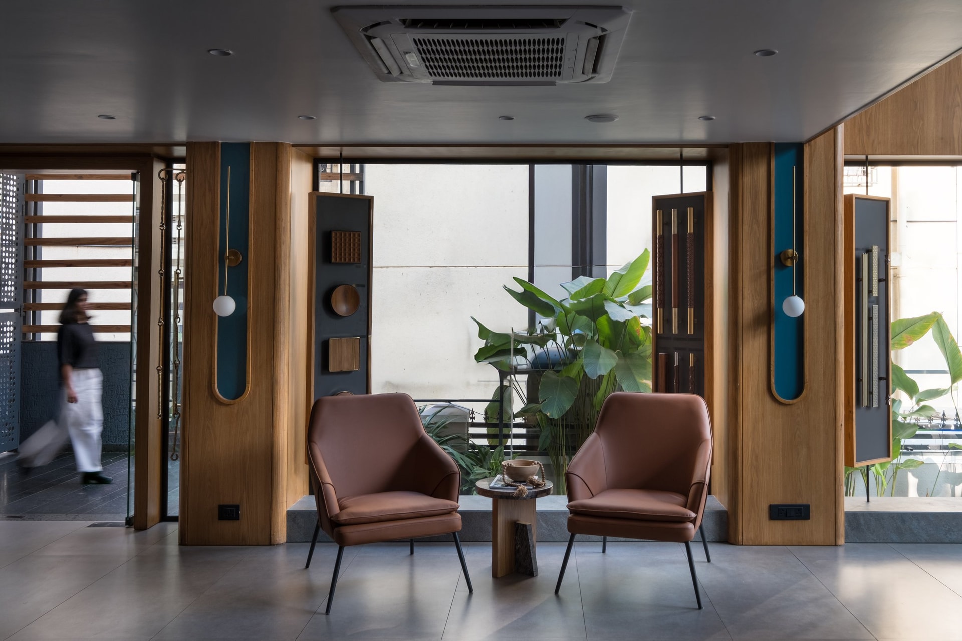 The threshold lounge: tan leather armchairs framed by oak piers and teal-backed niches set a residential register for what follows