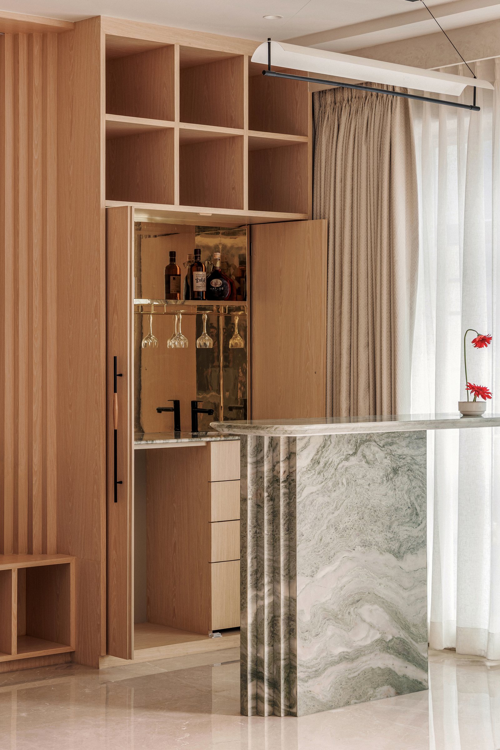 The bar unit, where a marble counter cantilevers out and an ash cabinet opens to a mirrored interior, storage, surface, and sculpture in one gesture