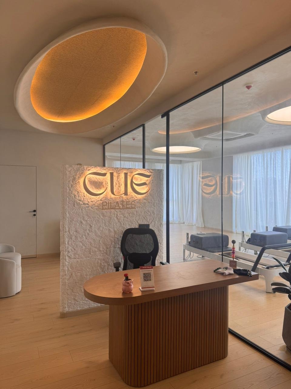 The reception desk, a reeded wood-grain oval set against the textured signage wall, with the practice floor visible through a glass partition