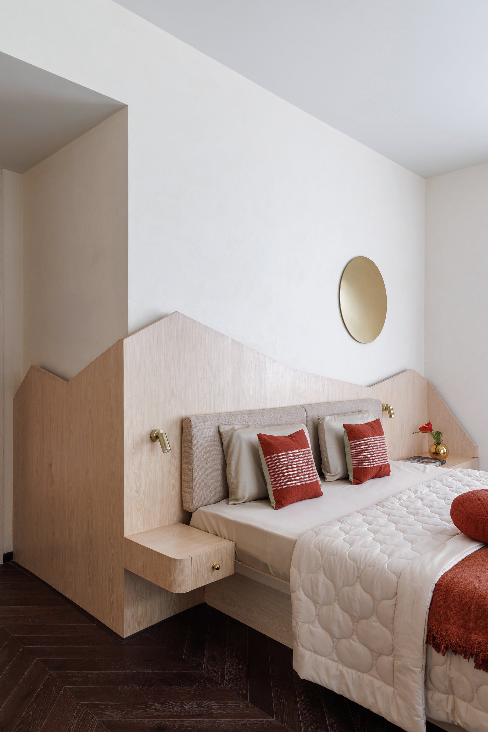 The integrated headboard wraps around the bed and steps down on either side to become side tables, then continues as wardrobe paneling beyond