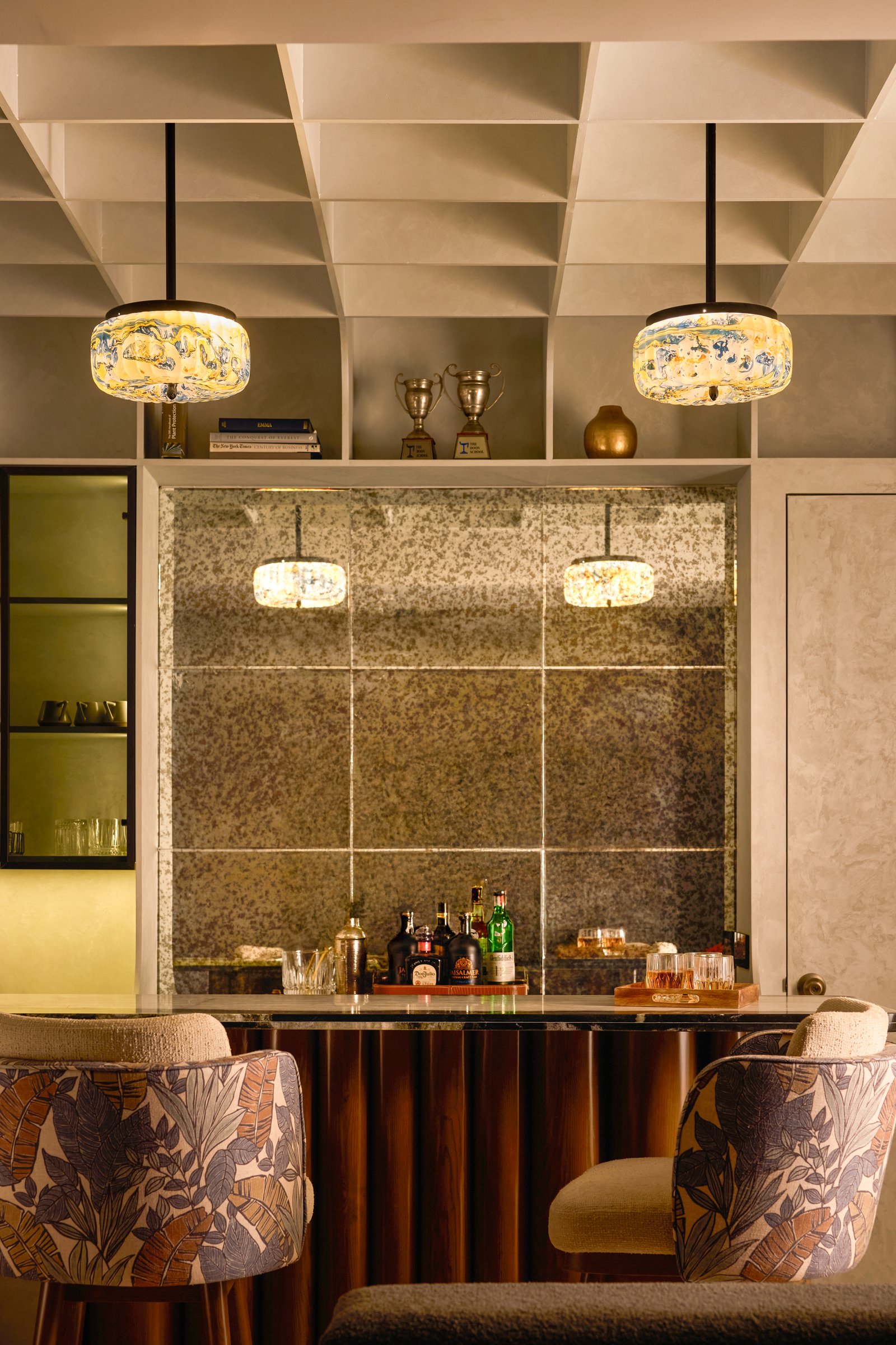 Beneath the coffered plaster ceiling, marbled-glass pendants frame the antiqued mirror panel of the bar