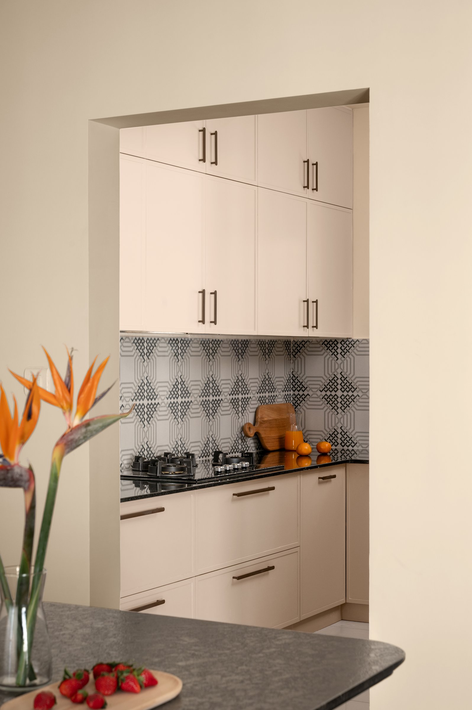 The kitchen, glimpsed through a clean rectangular opening, where a patterned backsplash provides the home's single moment of graphic energy