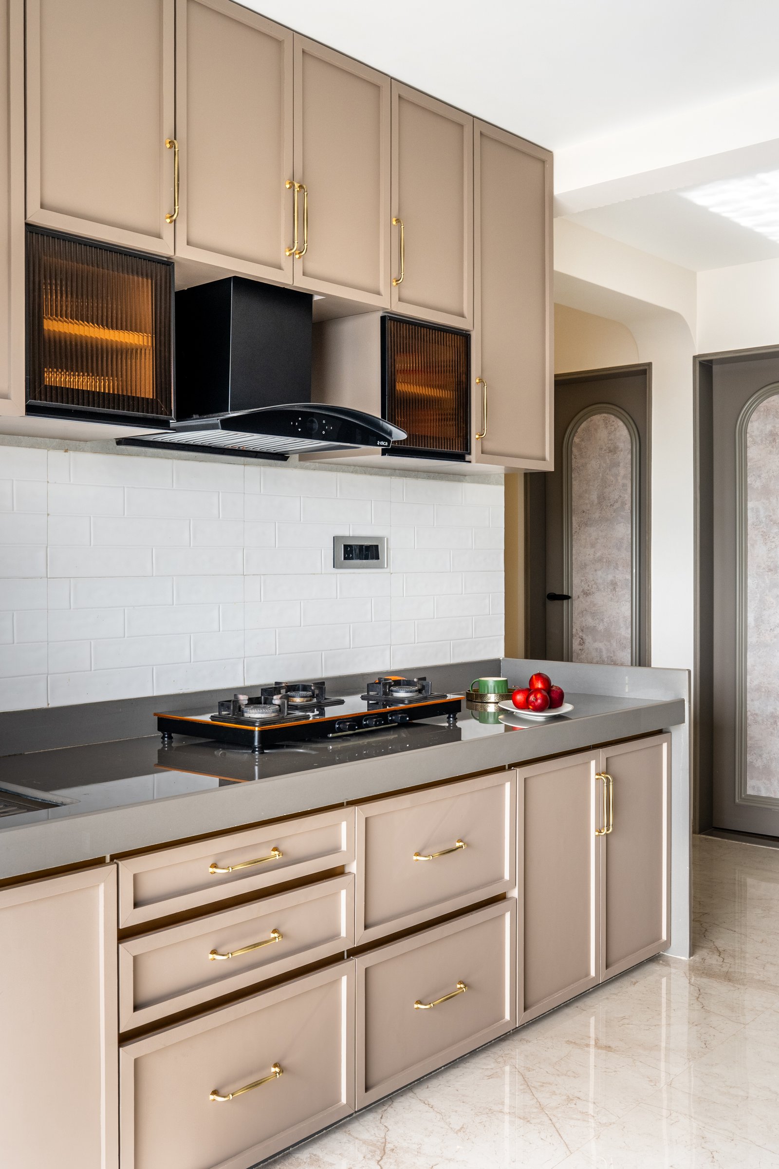 The kitchen, where dune-beige cabinetry and brass pulls warm a working surface that could otherwise read as clinical