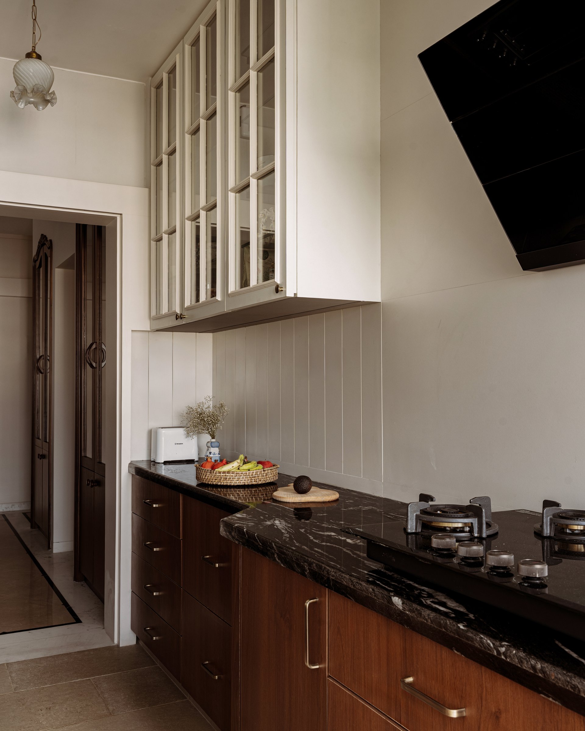 The cooking run, where glass-fronted upper cabinets and a veined black stone counter carry the home's discipline into its most utilitarian room