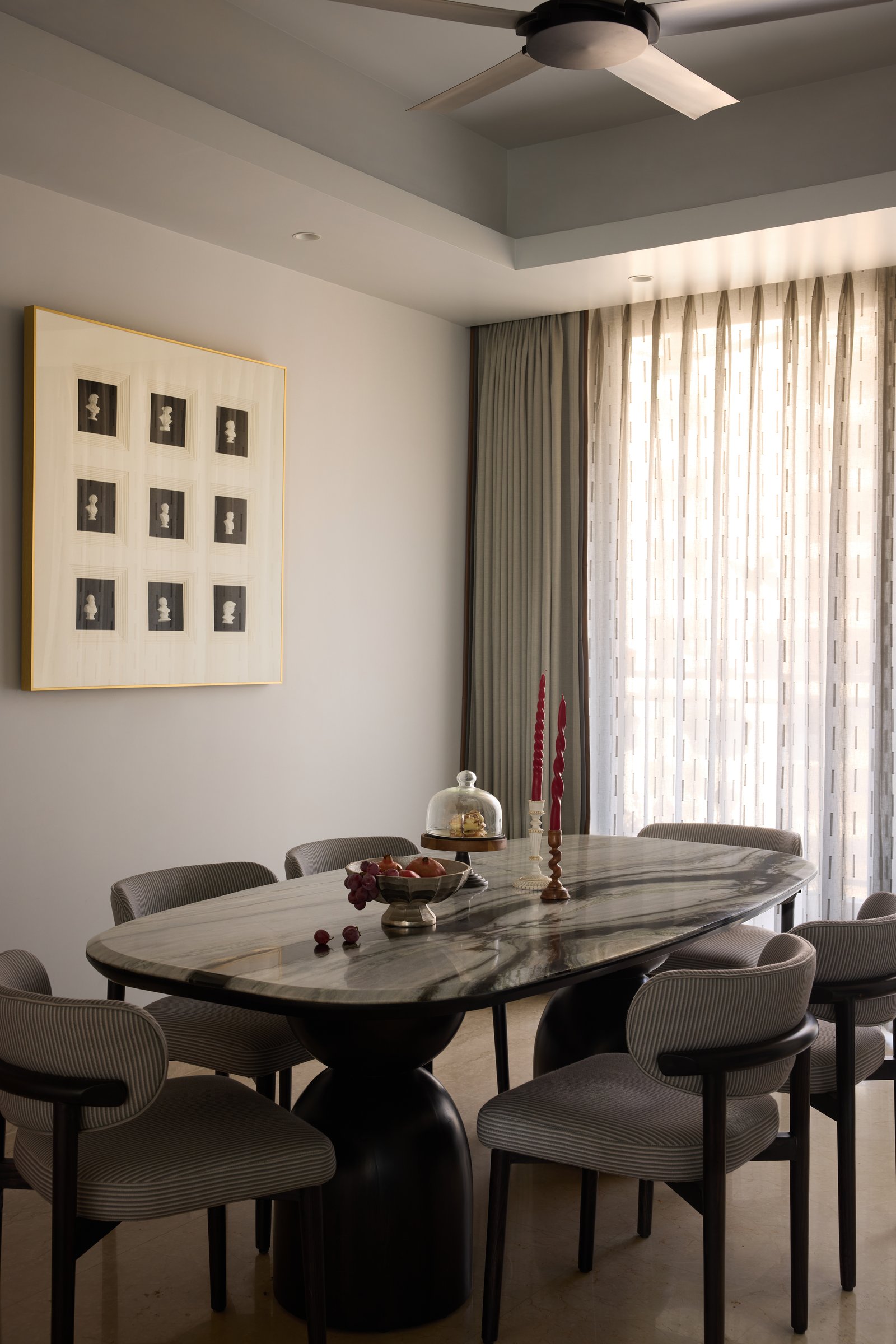 The dining area: an oval stone-topped table on a sculpted dark pedestal, with a sepia portrait grid alongside
