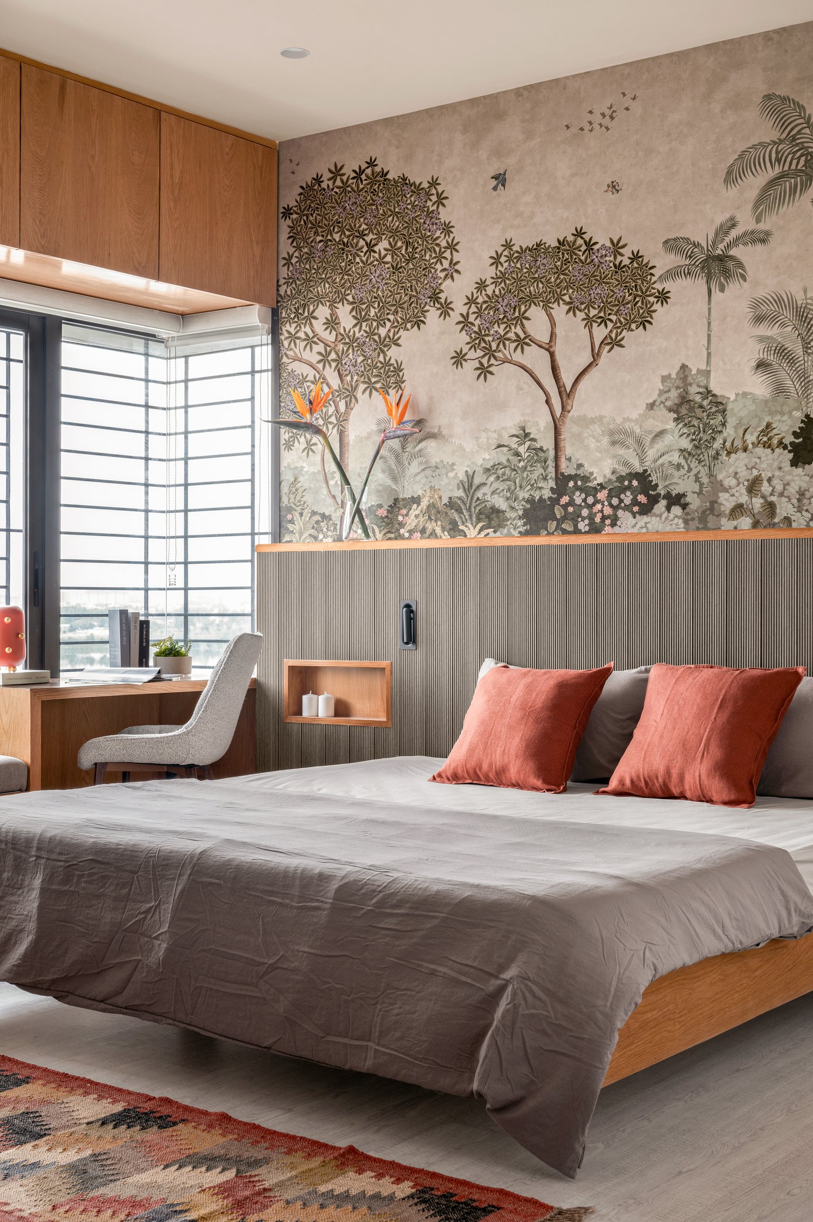 The master bedroom: a botanical mural and a fluted wood panel meet at a ledge where birds-of-paradise echo the bed's rust cushions