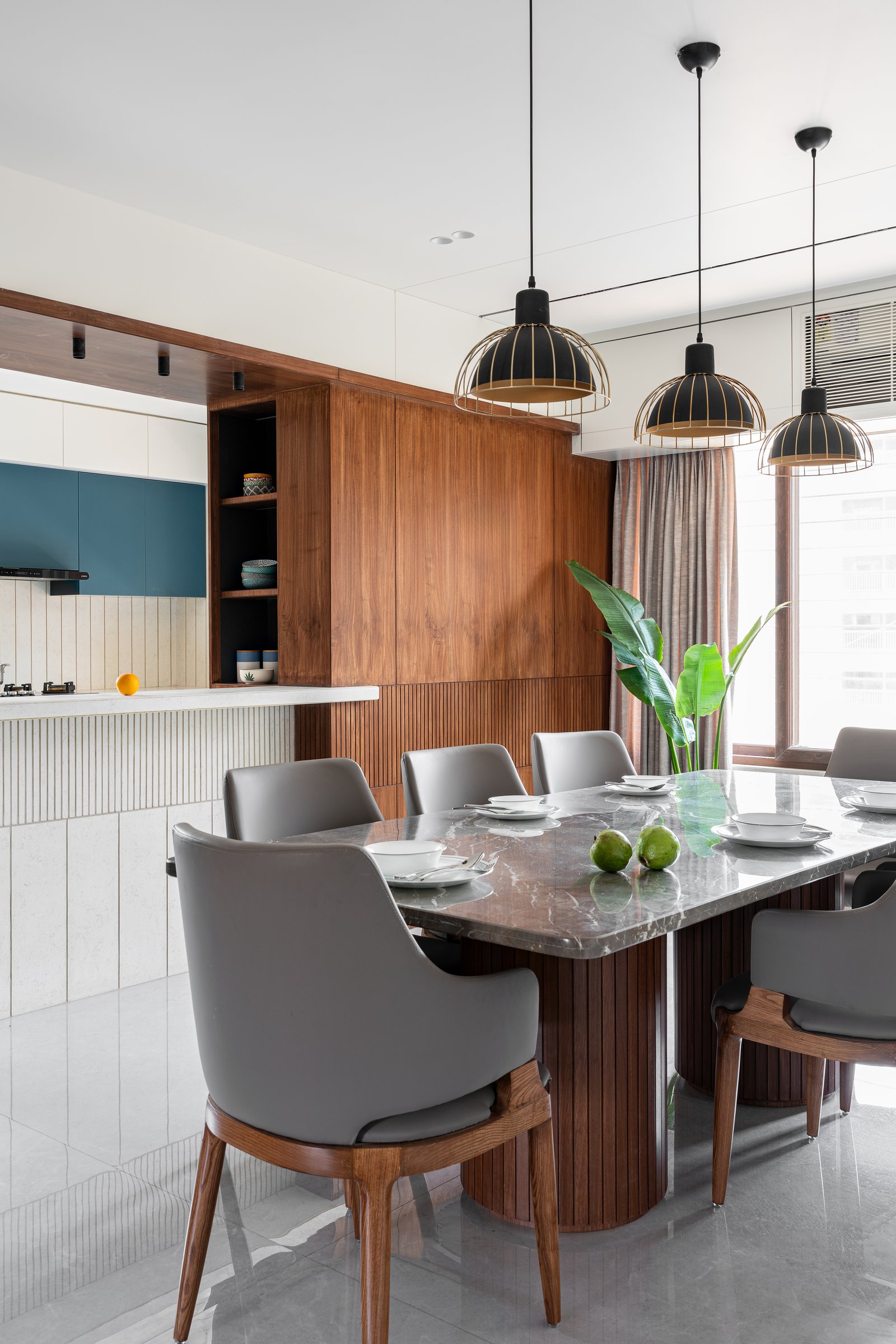 The on-site crafted dining table, its veined stone top echoing the floor, sits beneath cage pendants in matte black and brass