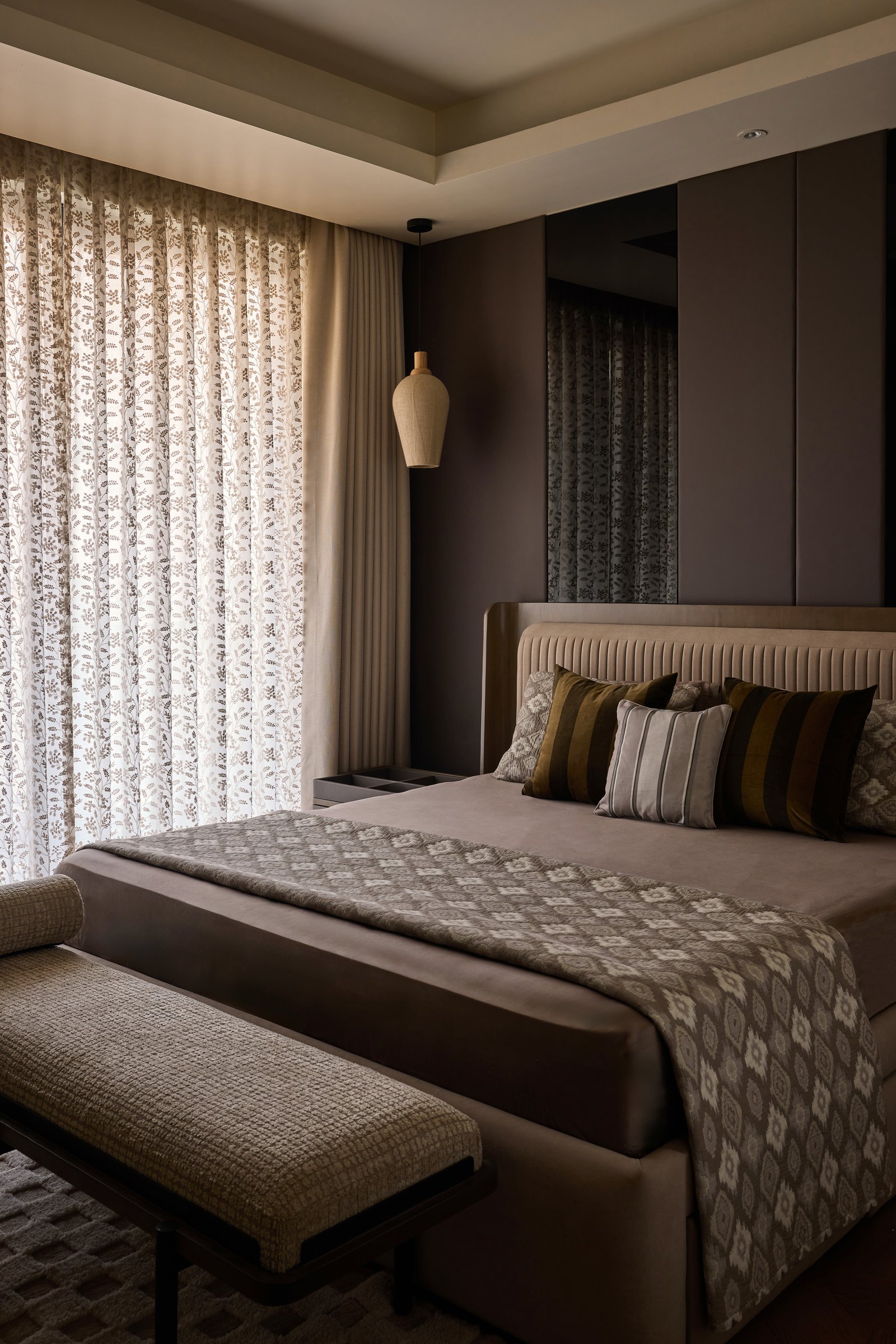 The first bedroom: a channel-tufted taupe headboard, dark panelled walls, and a jute pendant suspended beside the bed