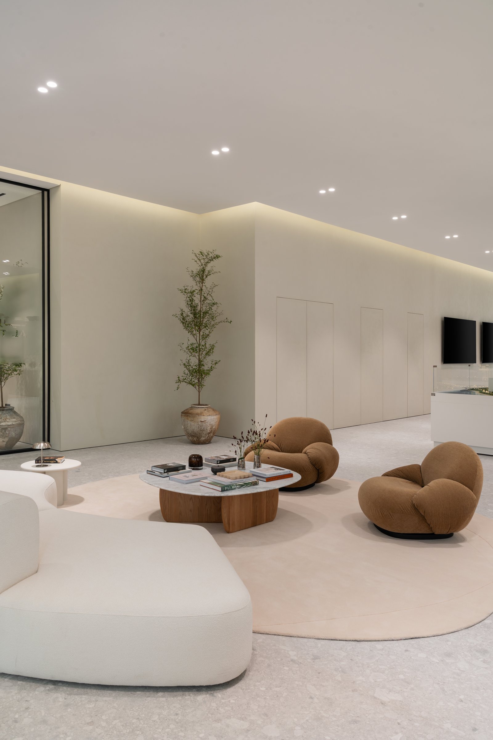The first guest seating hub: camel-toned Gubi Pacha chairs and a curved cream sofa gathered around a marble-and-oak table