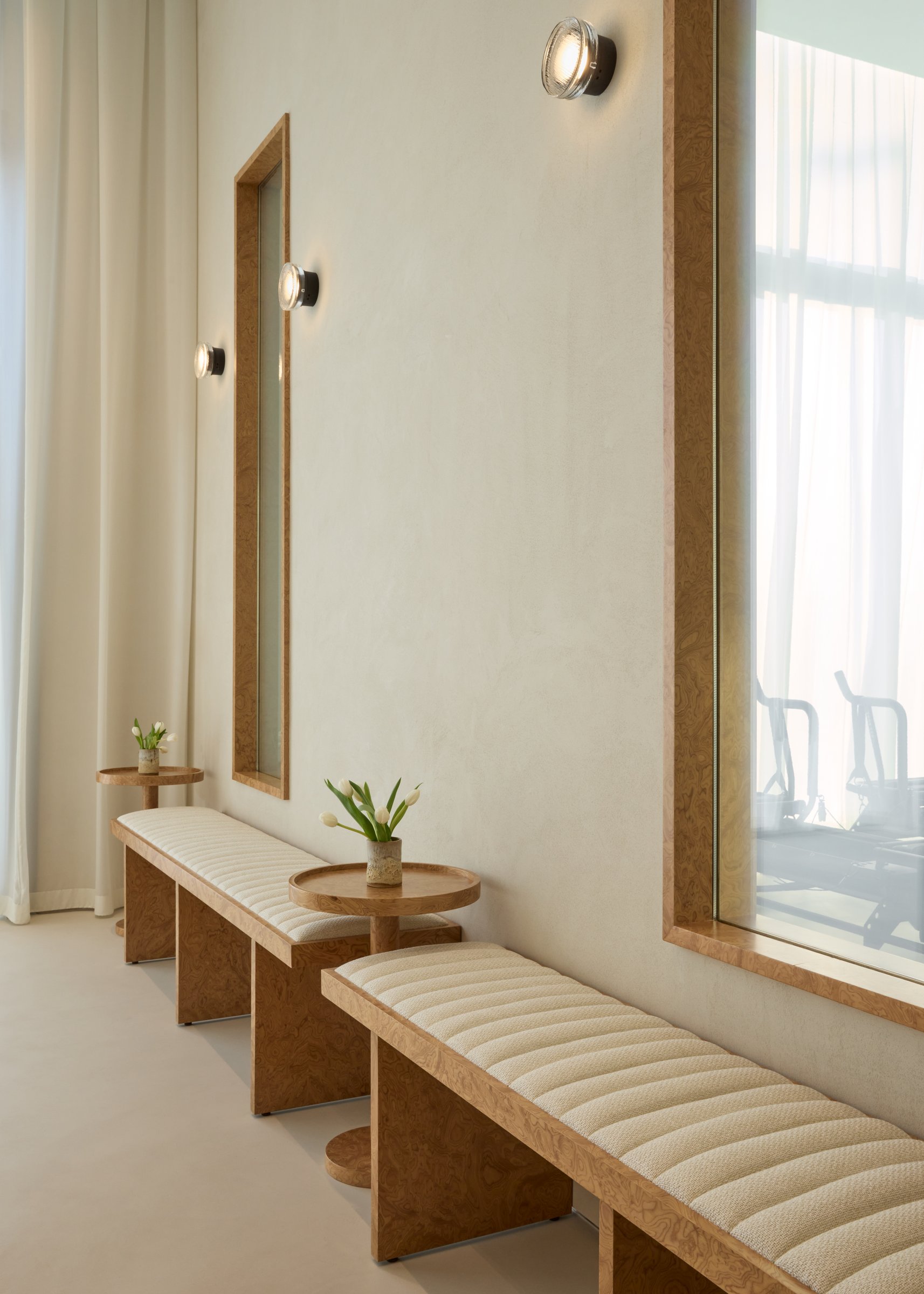 A run of burl wood benches lines the corridor outside the Lagree studio, with Marset sconces punctuating the micro-cement wall