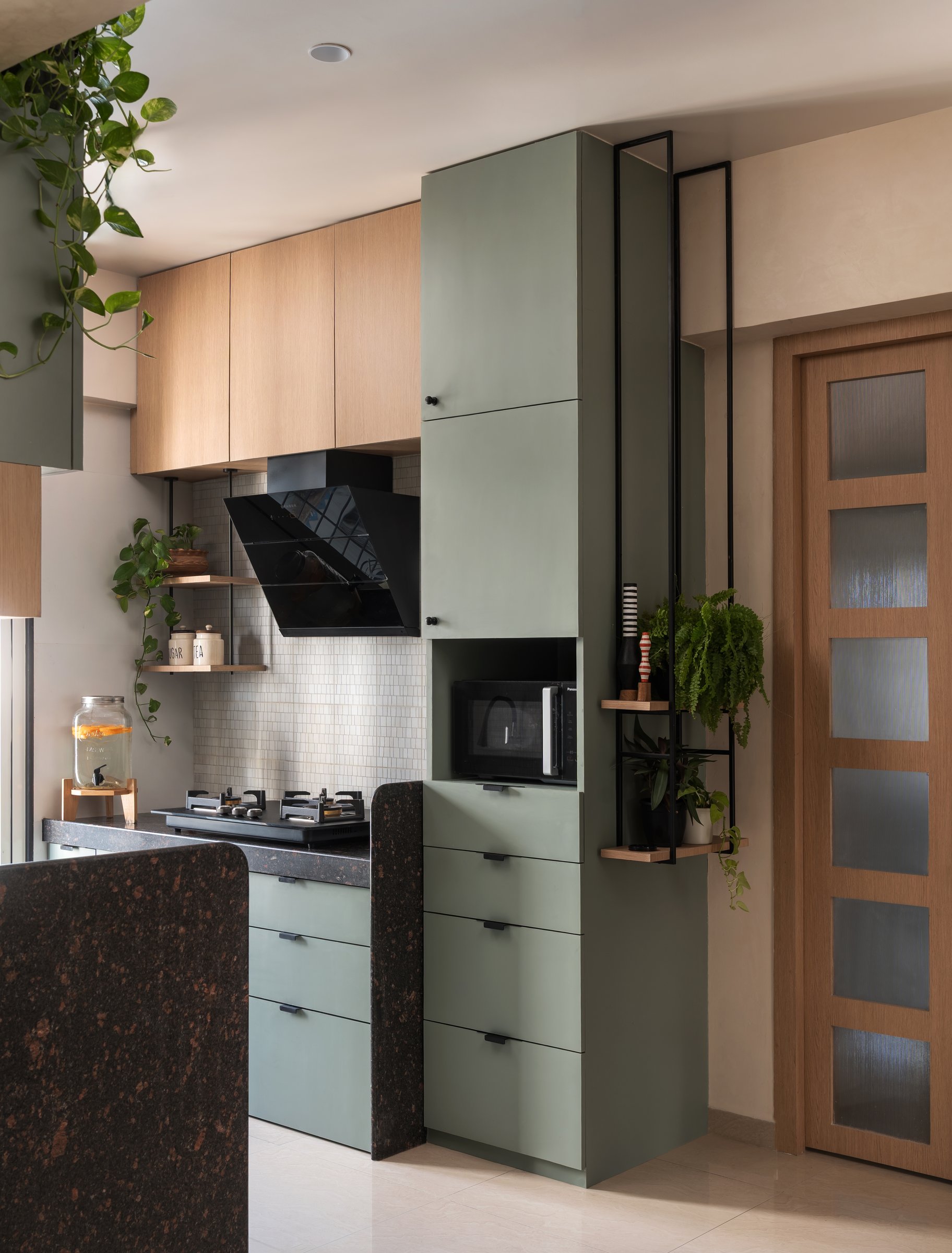The working side of the kitchen: a sage storage column with an integrated microwave niche and a slim metal shelf for trailing greens