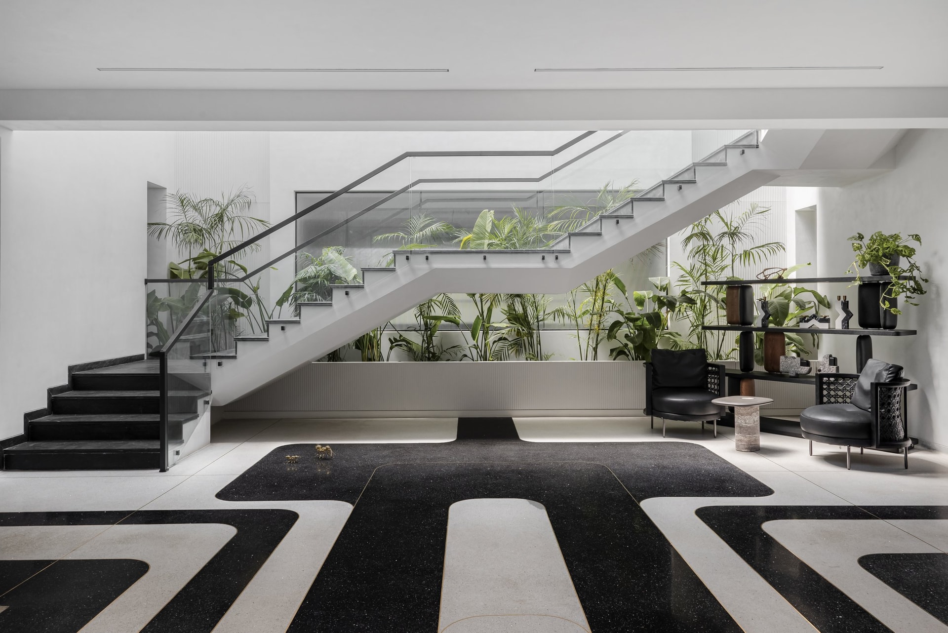 The double-height foyer, where a graphic terrazzo floor and a glass-balustered staircase set the home's spatial language