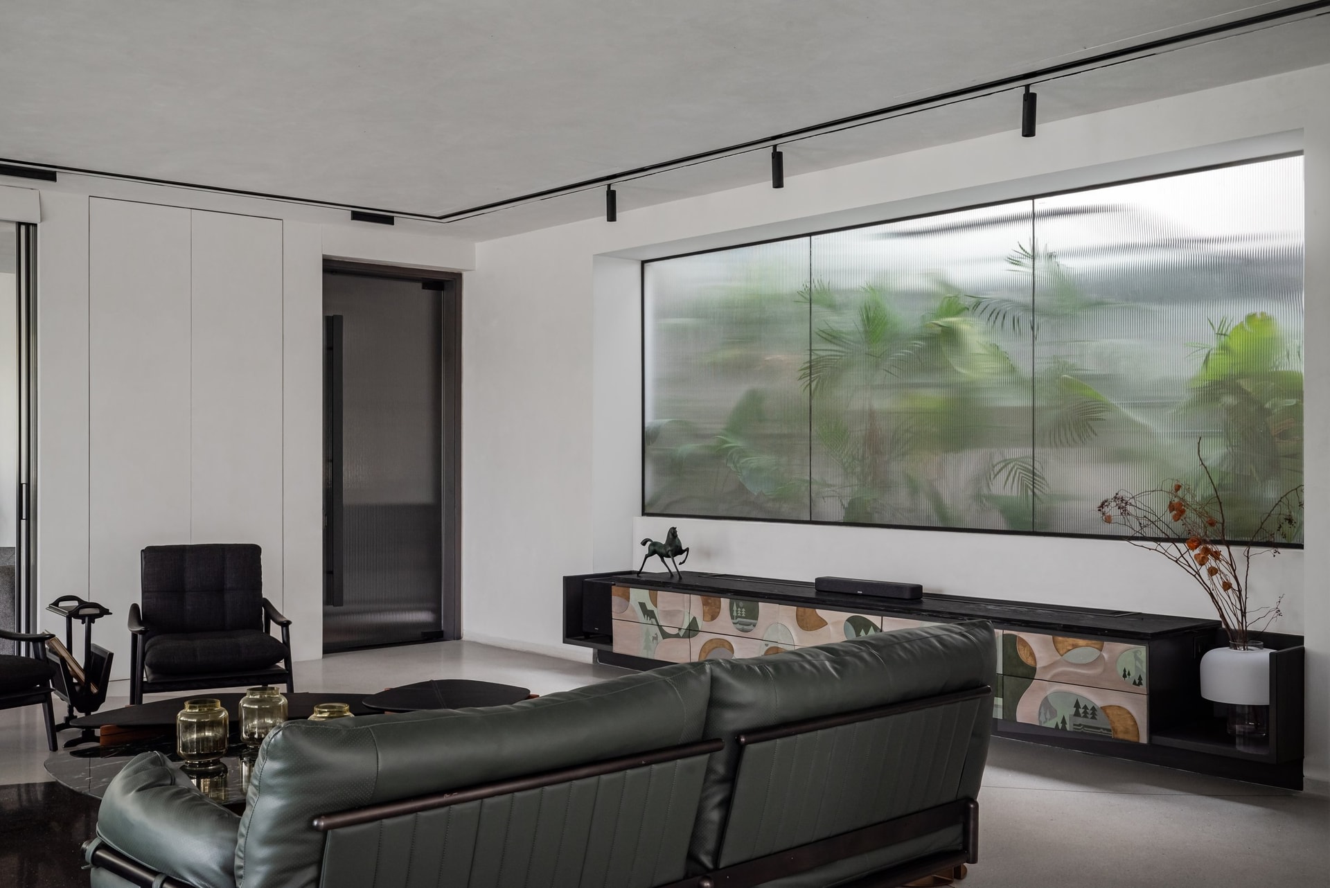 A long painted console runs beneath a fluted glass aperture framing the planted courtyard