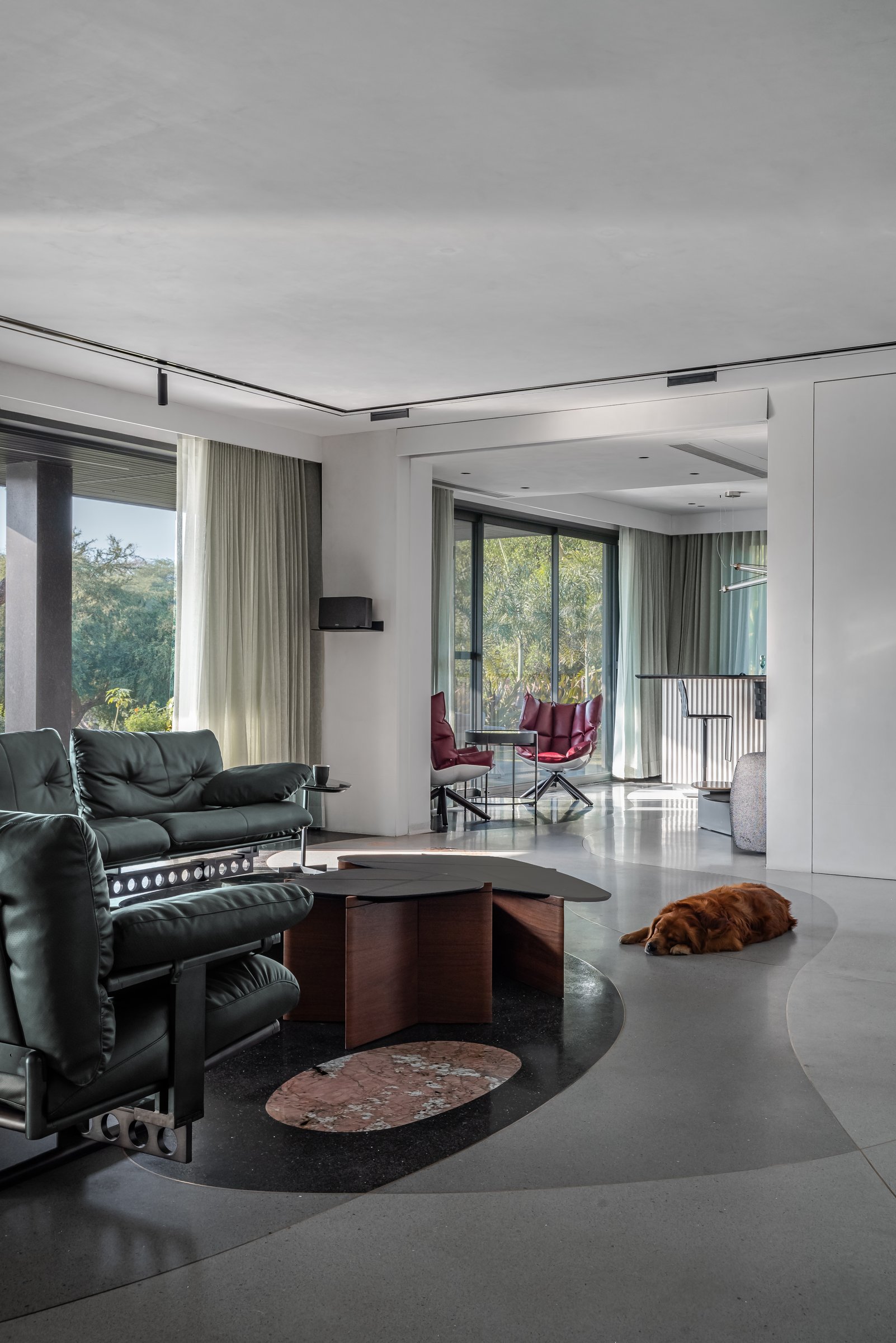 The living room opens to the garden through floor-to-ceiling glazing, the curved floor inlay quietly defining the seating