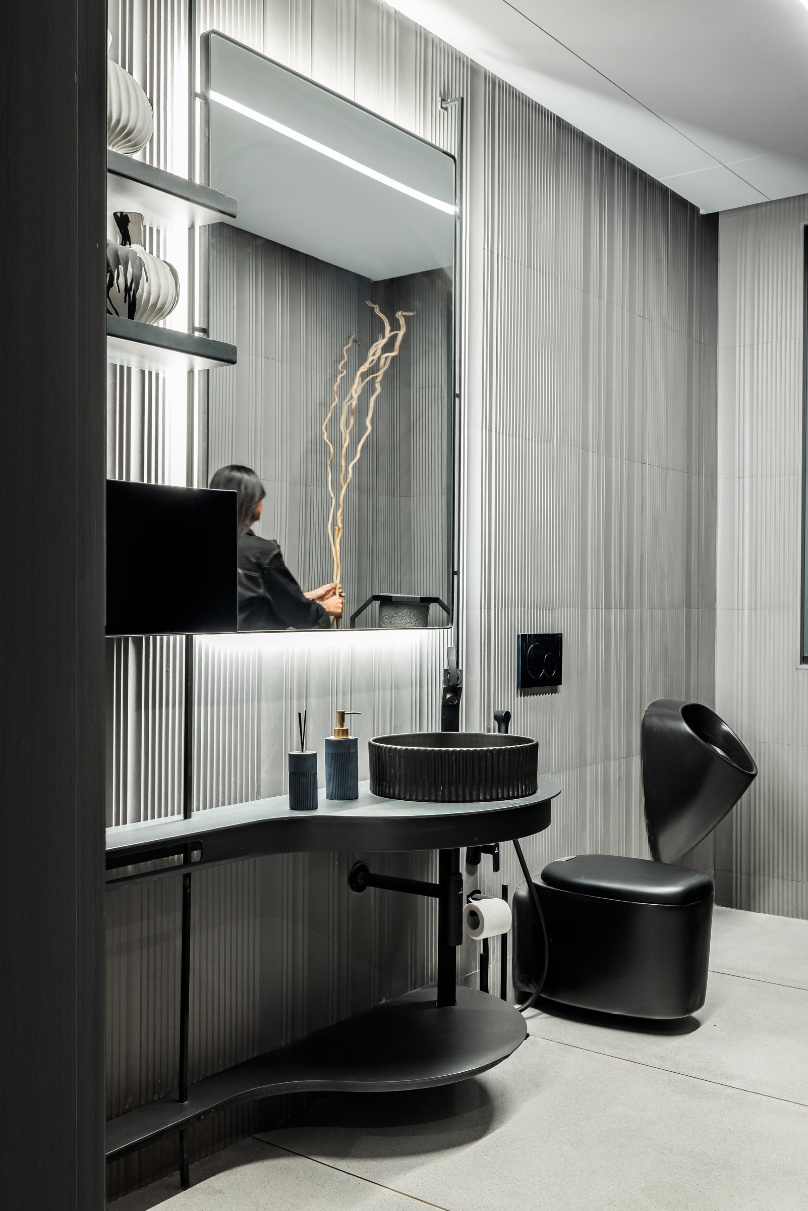 A second bathroom in fluted grey tile, with a sculptural ribbed basin on a curved vanity