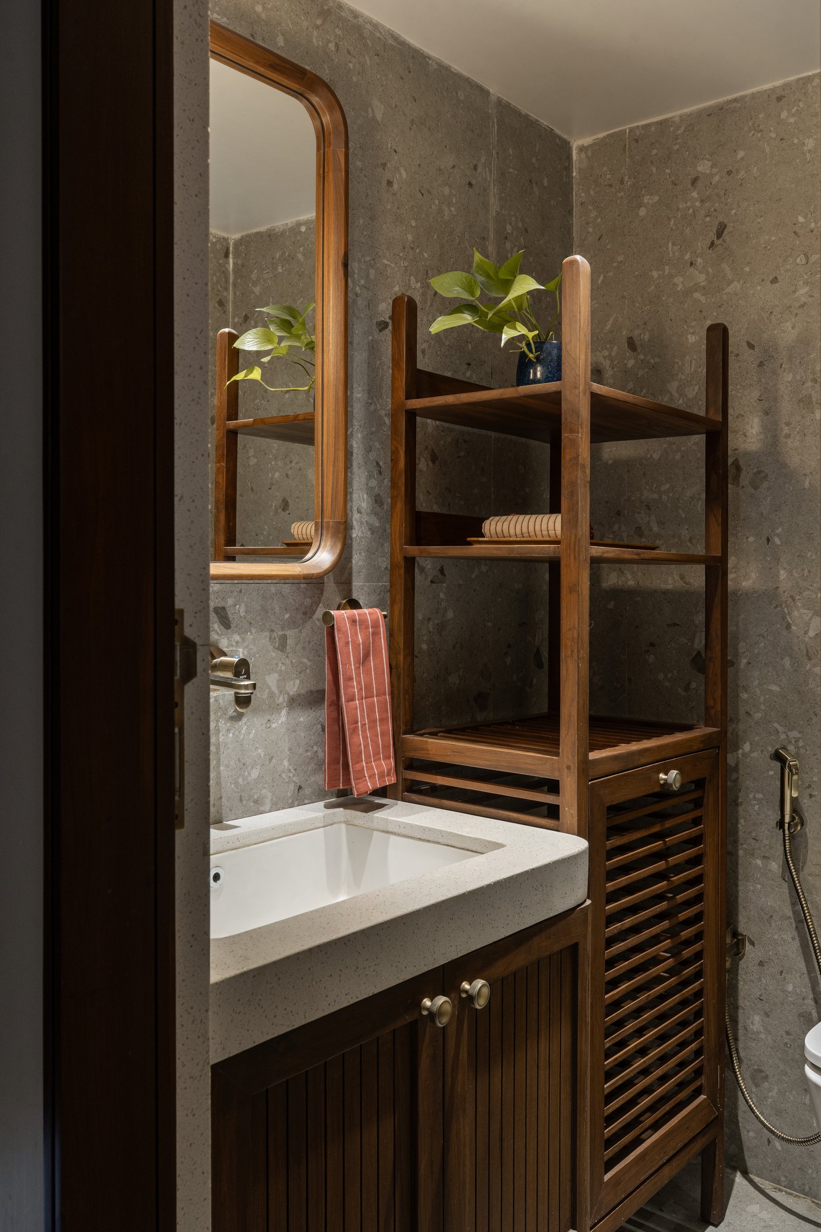 The bathroom unifies shower and powder area in grey terrazzo, with a slatted teak tower and a rounded mirror echoing the home's curve language