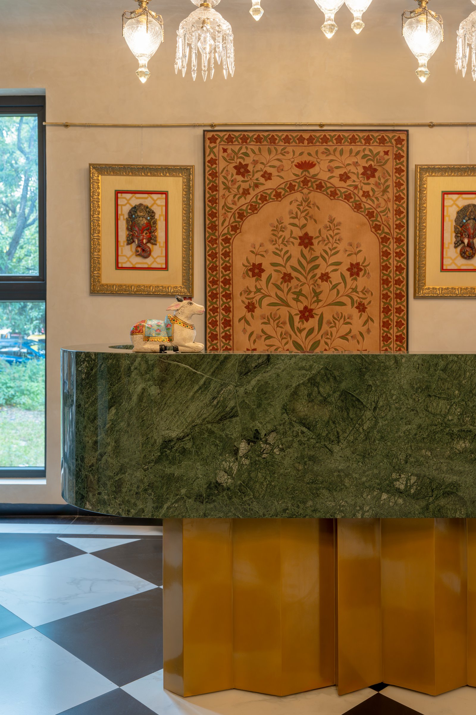 The reception counter: a curved green stone top resting on a fluted brass base, beneath a Mughal-inspired textile
