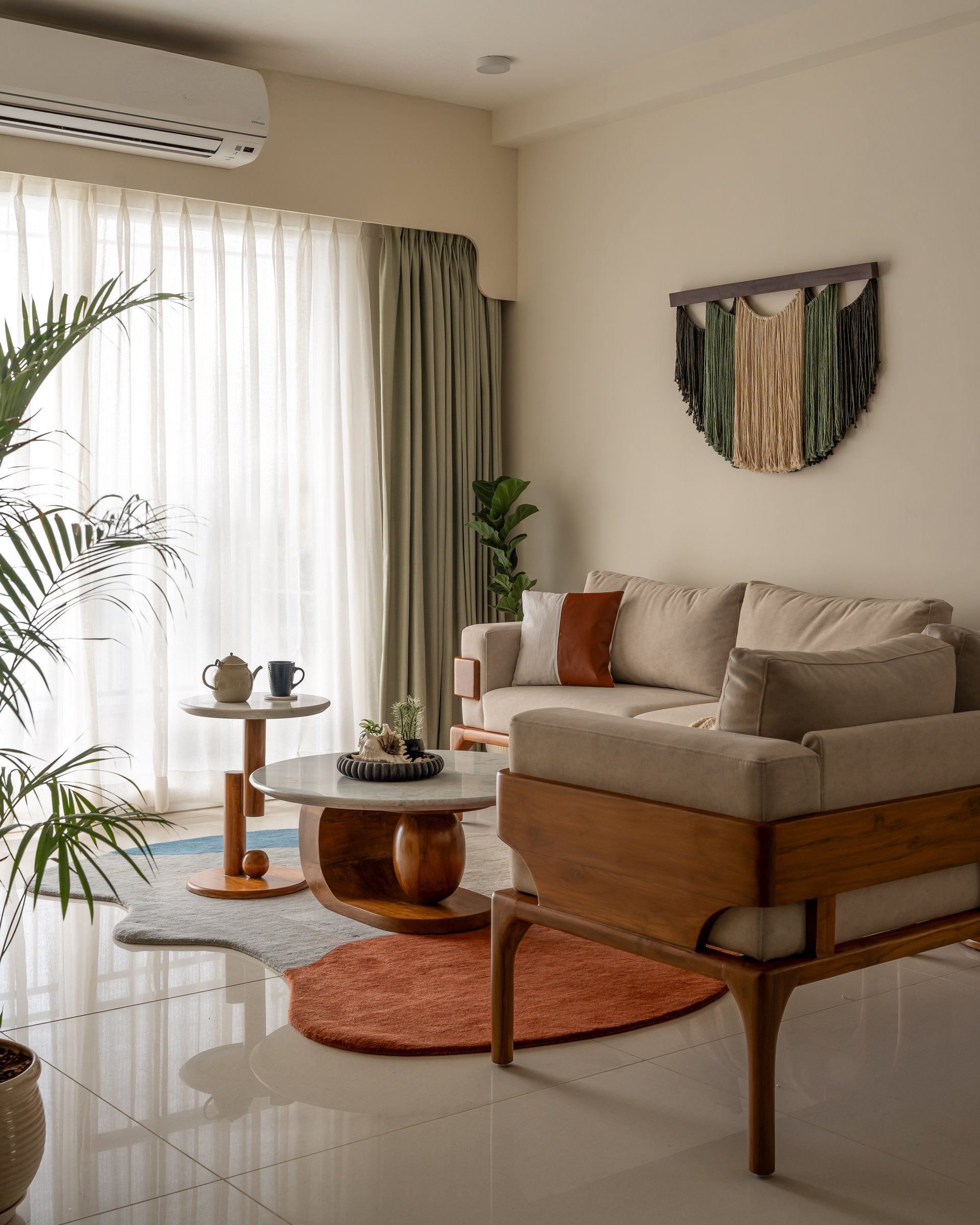 In the living room, a linen sofa and sculptural coffee table sit beneath a macramé hanging in sage and oat tones