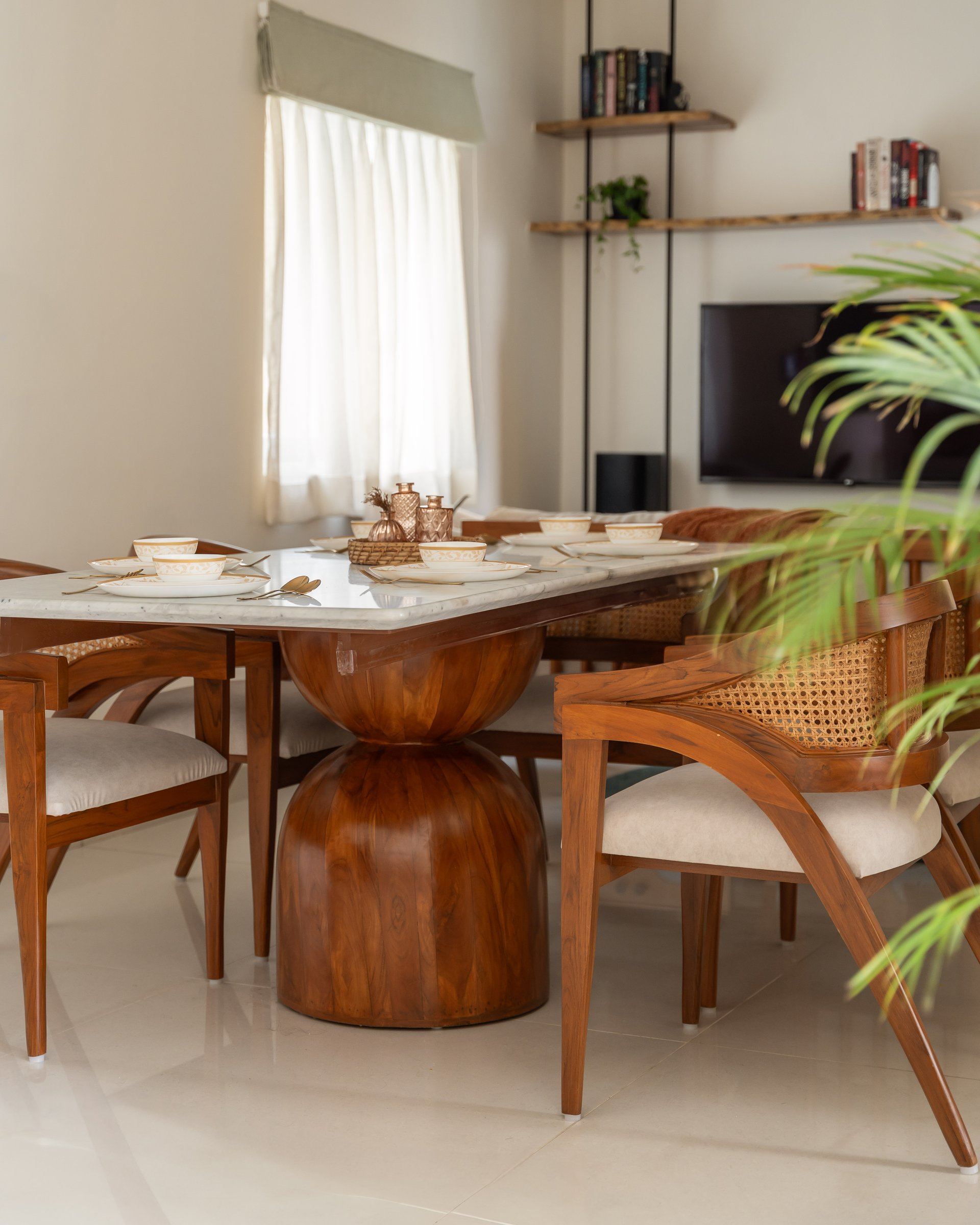 The dining table: a marble top on a sculpted wooden pedestal, surrounded by cane-backed armchairs