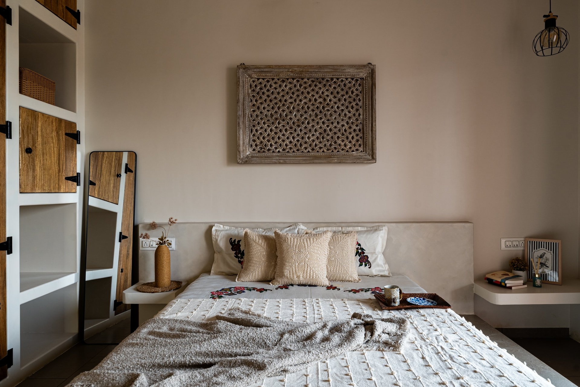 A salvaged carved jali panel becomes the room's single decisive gesture above the upholstered headboard