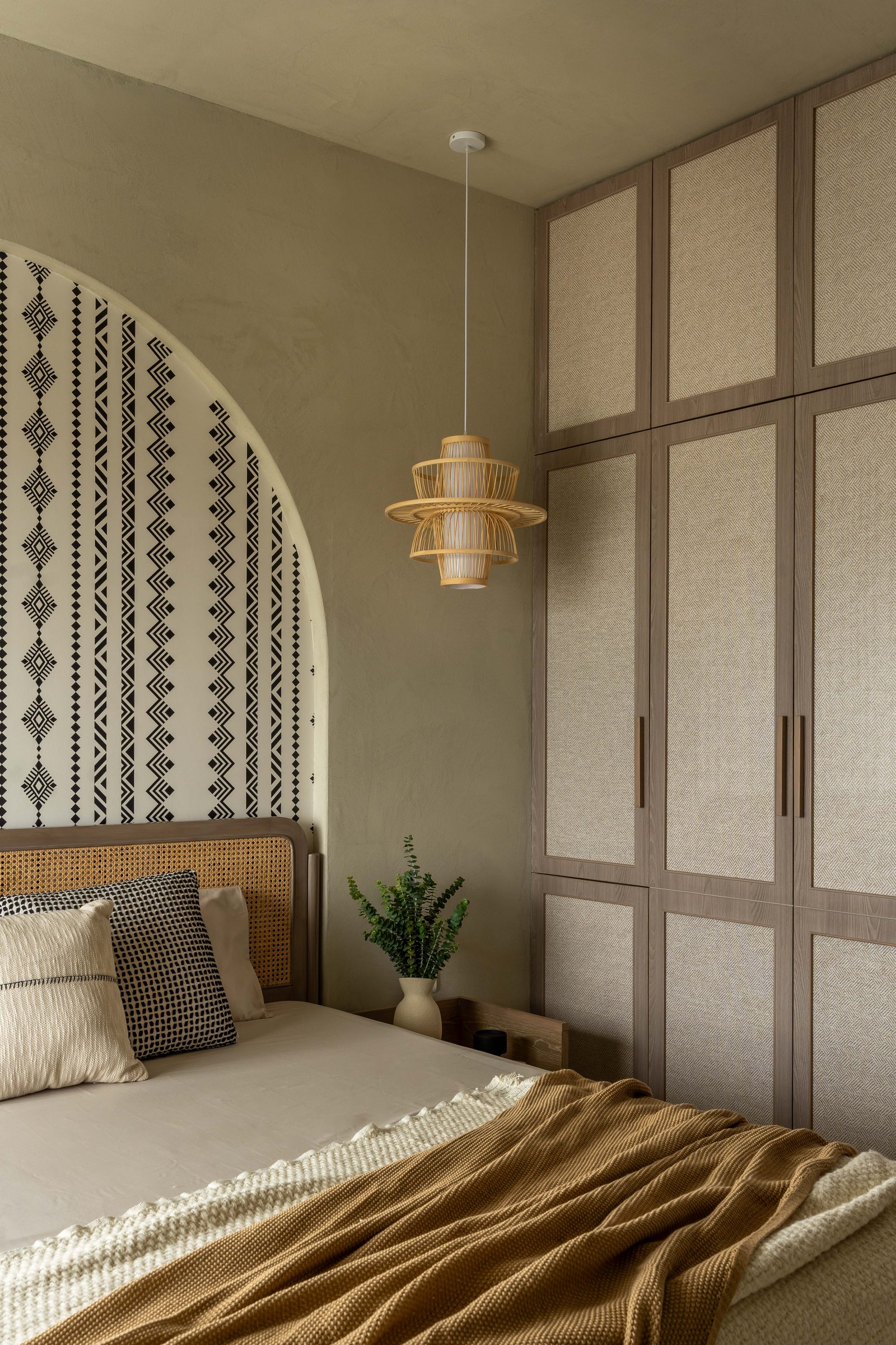 Herringbone-weave wardrobe doors and a tiered rattan pendant register the room's vertical proportion