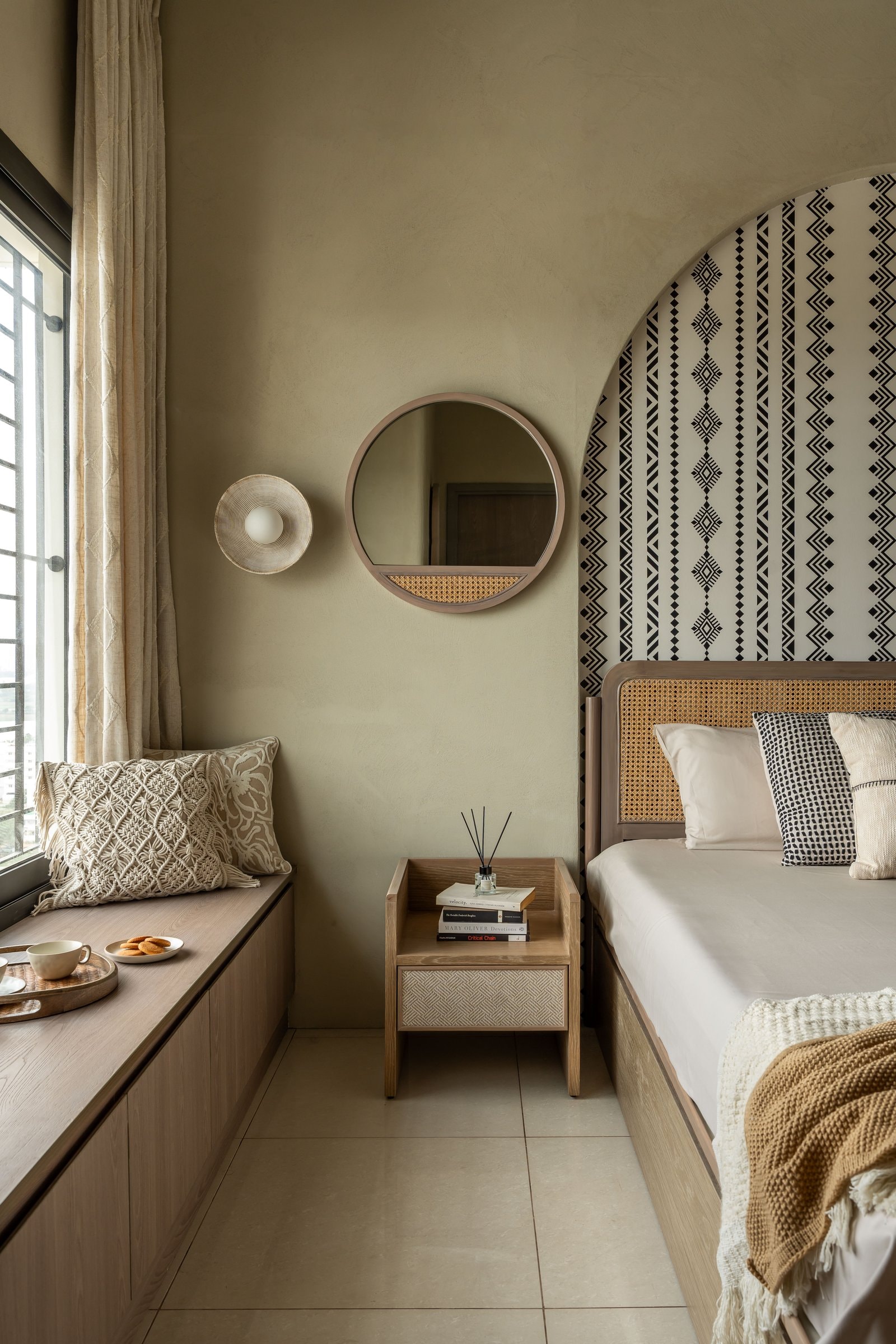 The window seat and circular caned mirror extend the bedroom's quieter life