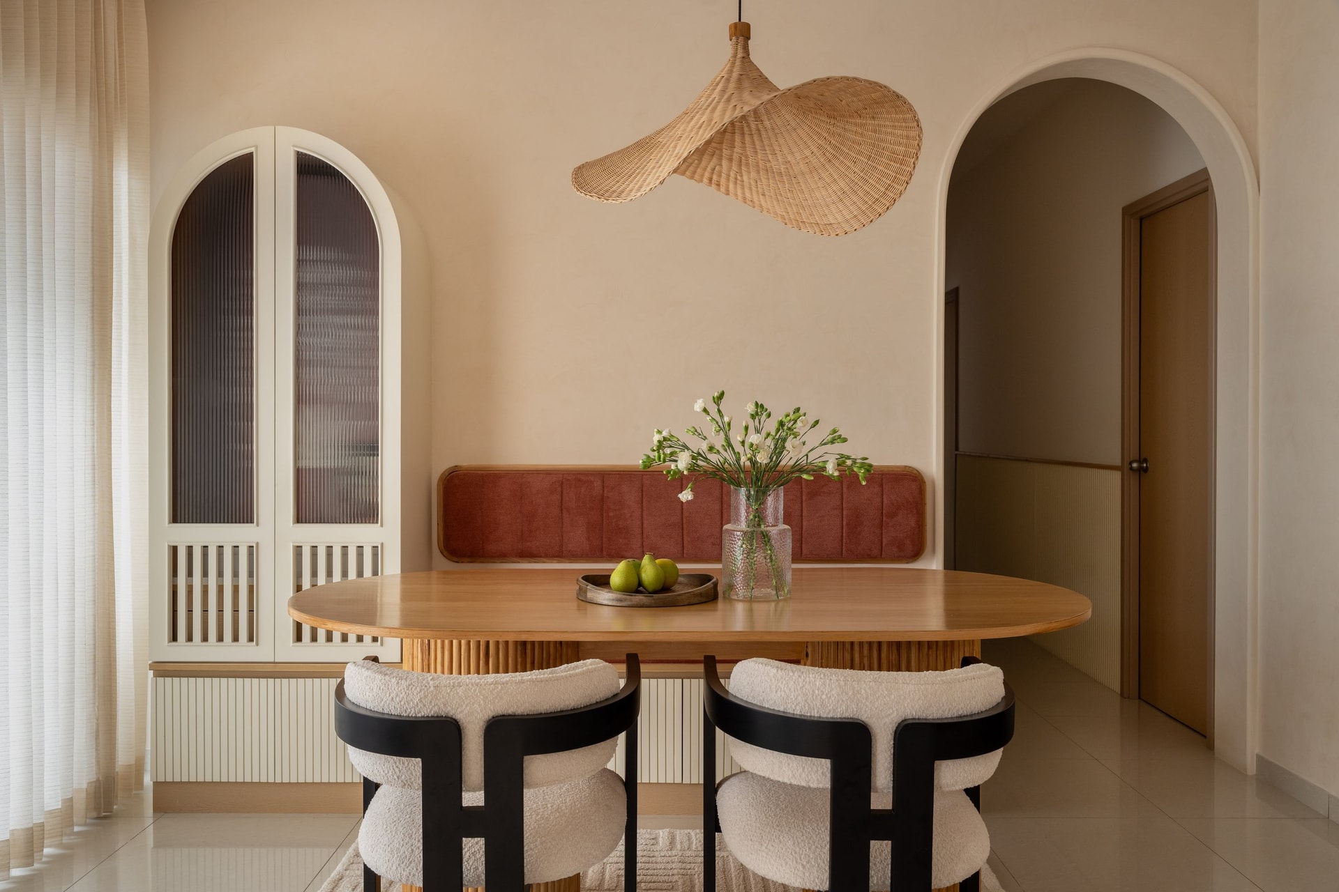 The dining area, where coral velvet, oak, and a sculptural rattan pendant make a quiet argument for warmth