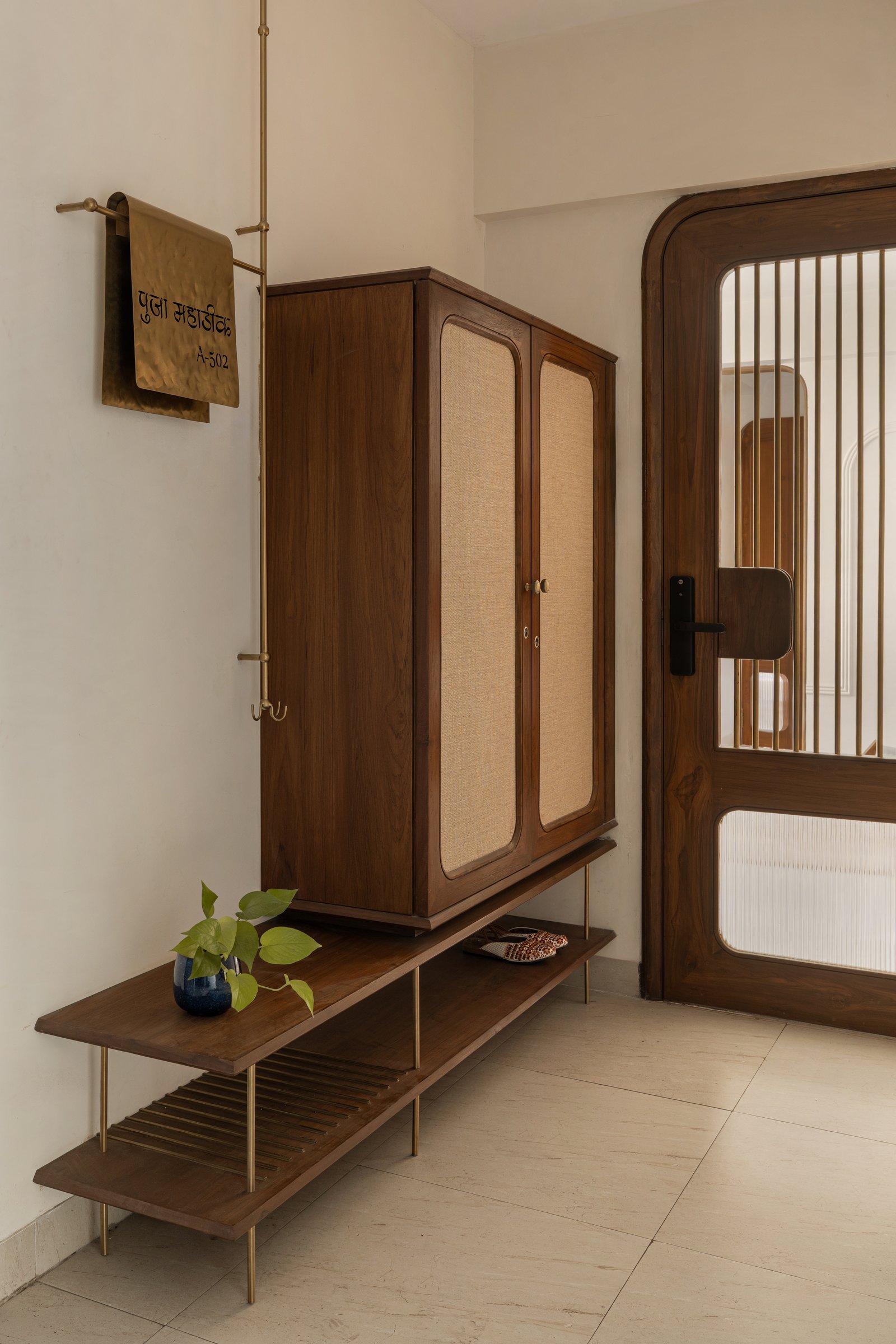The foyer: a teak console with a slatted shelf and a hammered brass nameplate set the home's material grammar at the threshold
