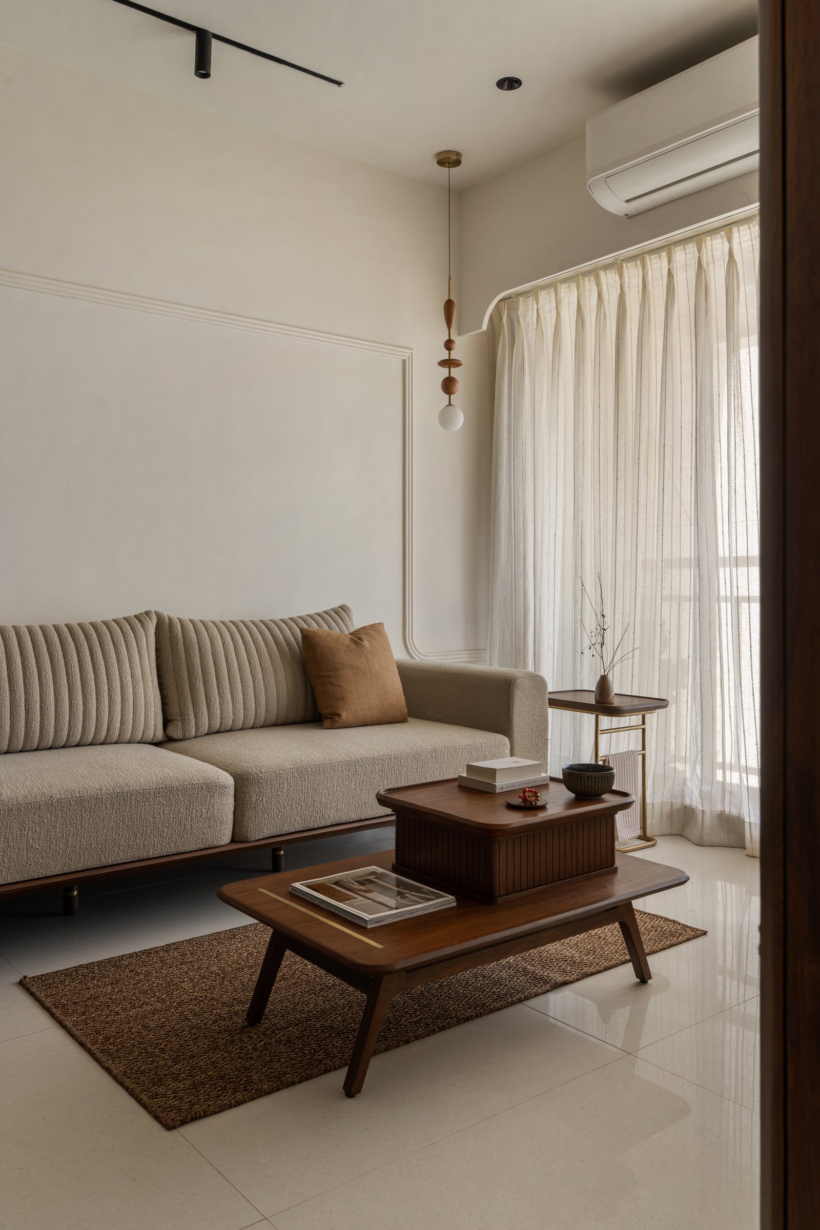 The living room, where continuous wall mouldings and a pair of nesting tables in dark teak create a hugging volume that doubles as low dining