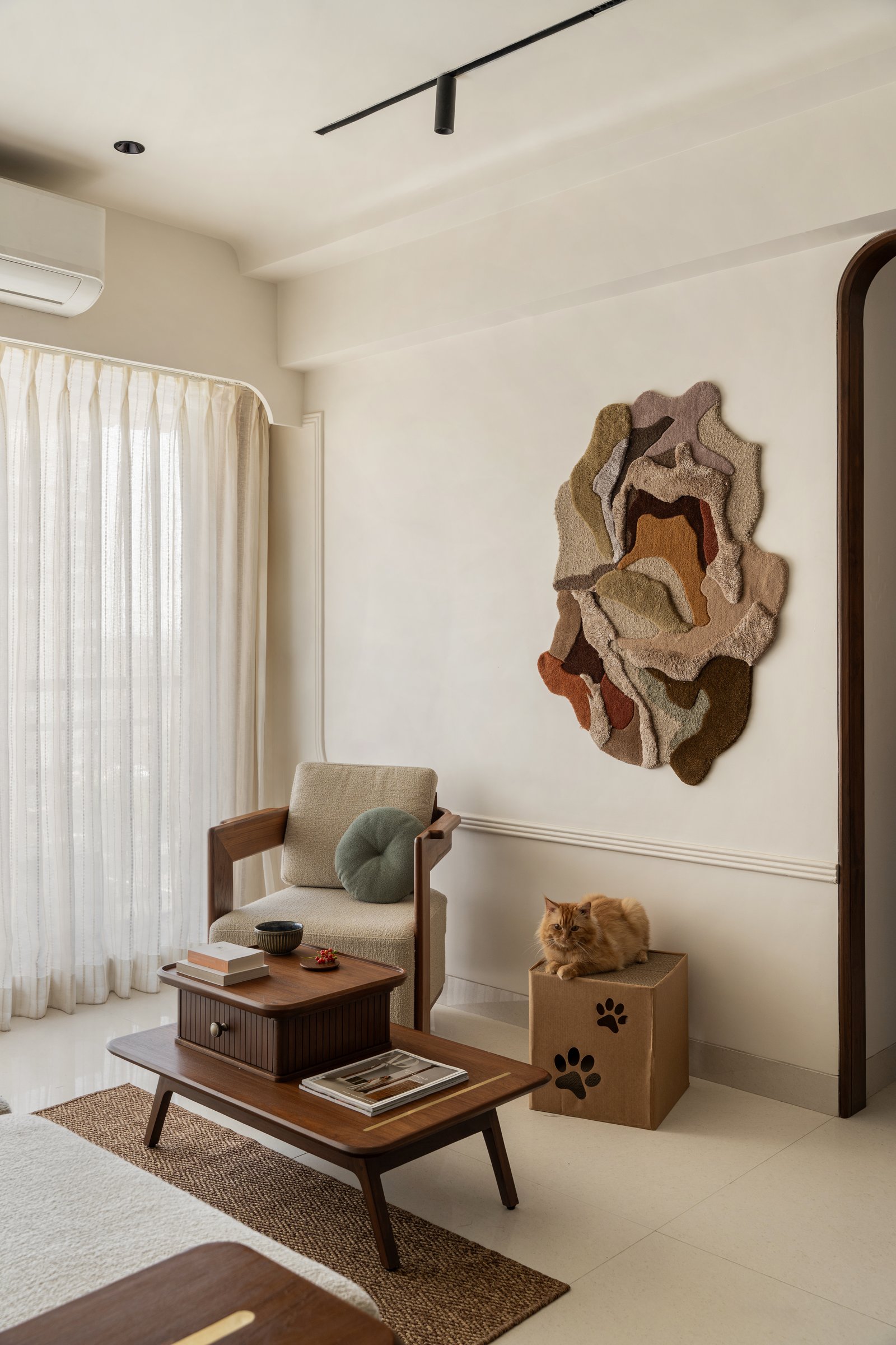 A bespoke wall rug in varying pile heights becomes the room's single decorative event, anchoring the seating zone beside the teak armchair