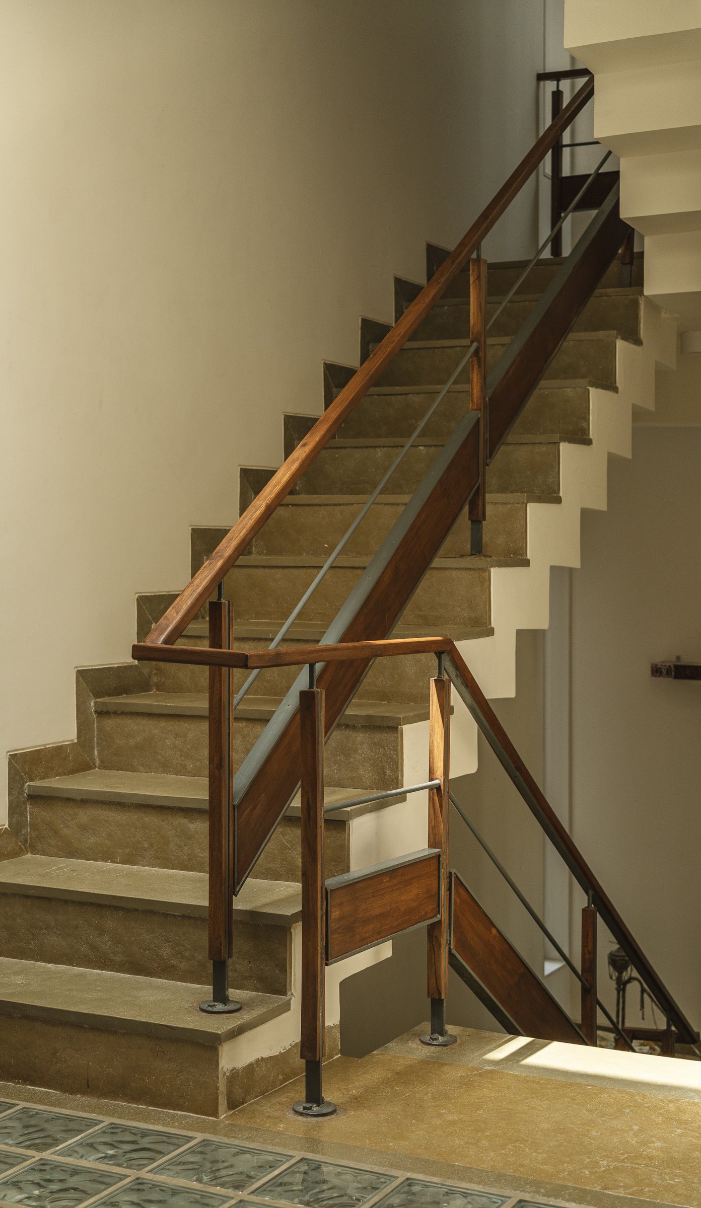 The staircase from below, where concrete treads meet a wood-and-steel handrail in a pragmatic, unfussy detail