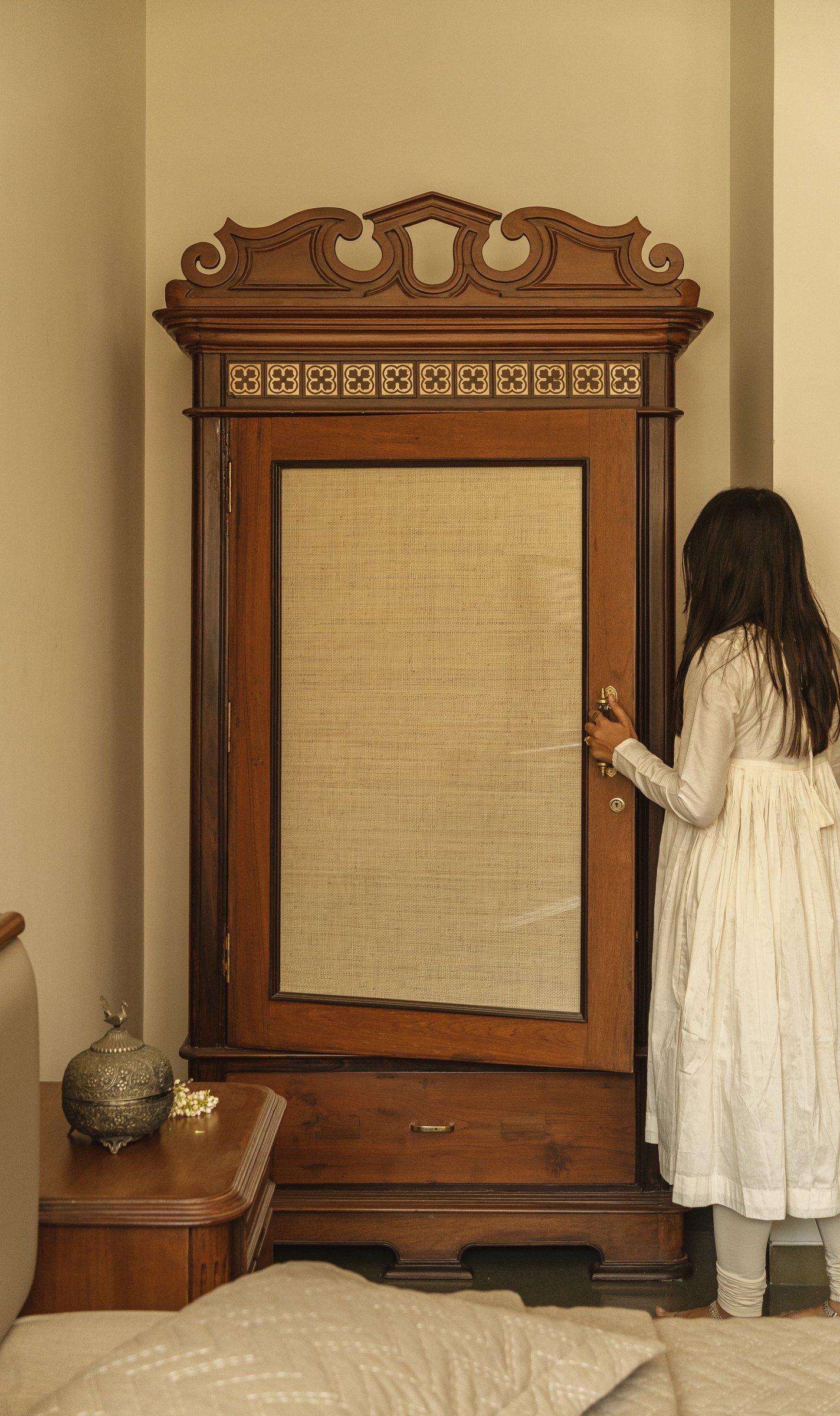 The heirloom almirah, with its carved pediment and caned central panel, given an unornamented stretch of wall