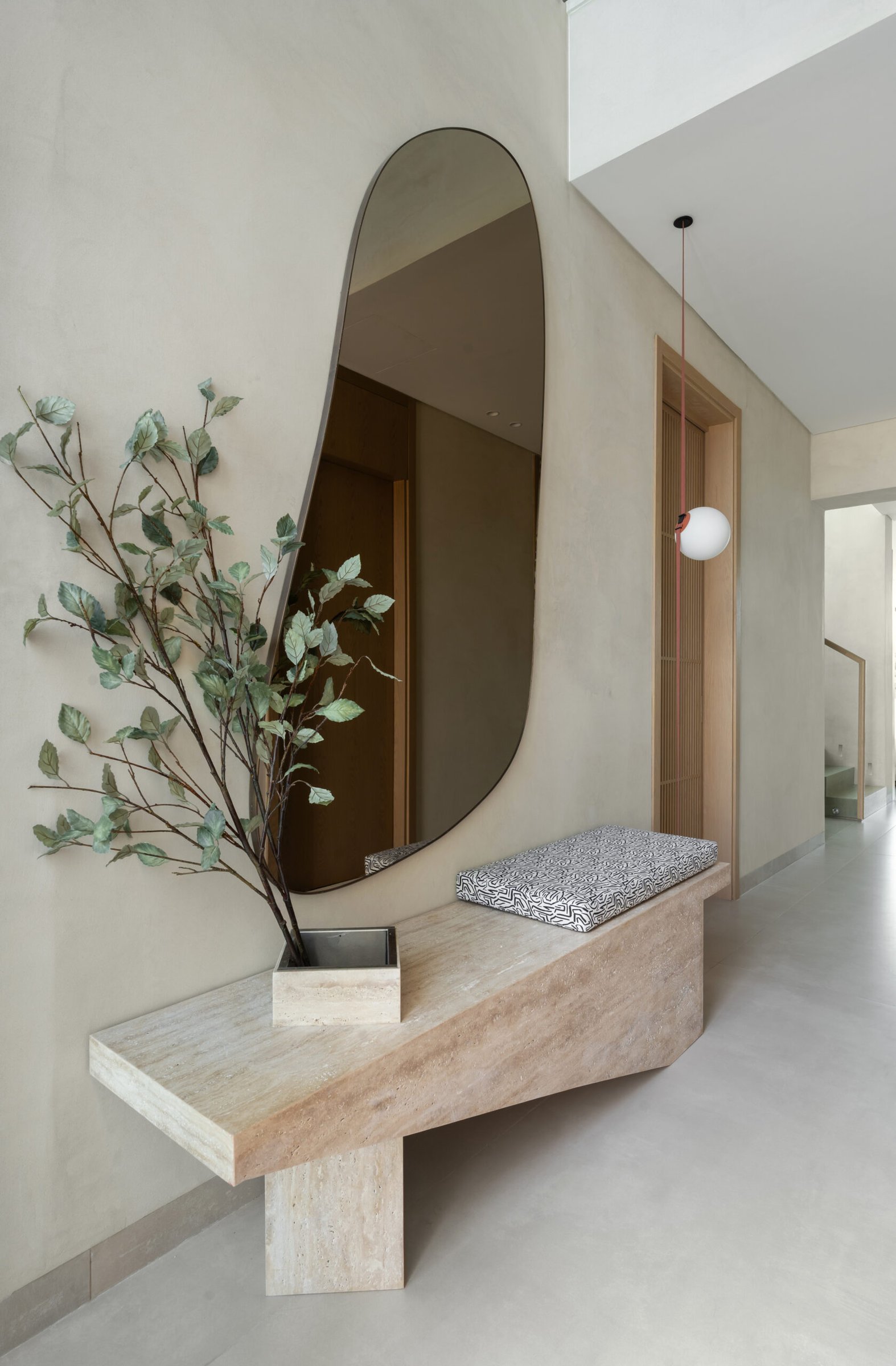 The foyer: a travertine console and asymmetric mirror set the home's tonal grammar before a single room reveals itself
