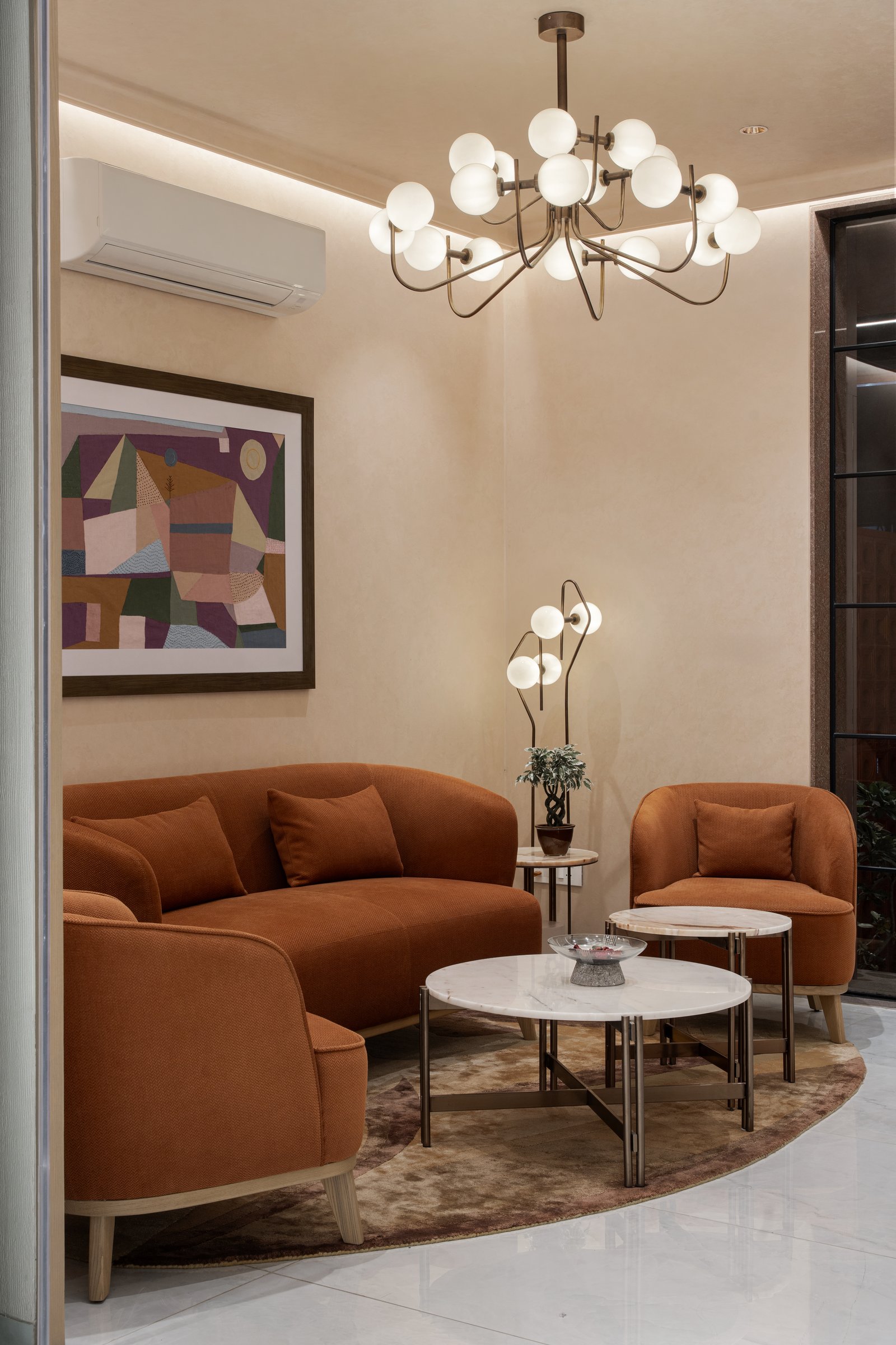 The waiting lounge: the project's one moment of chromatic warmth, in deep rust upholstery beneath a multi-globe brass chandelier