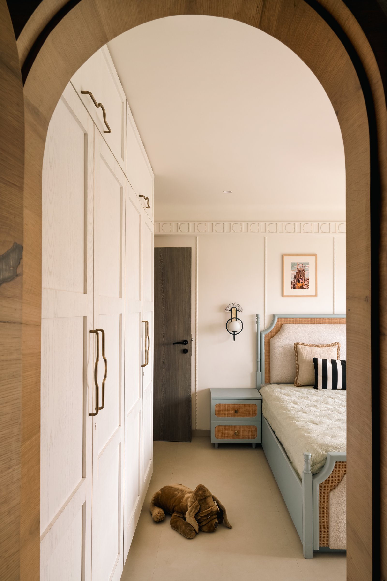 Viewed through a tall wooden archway, the second daughter's room continues the cream-and-dusty-blue palette