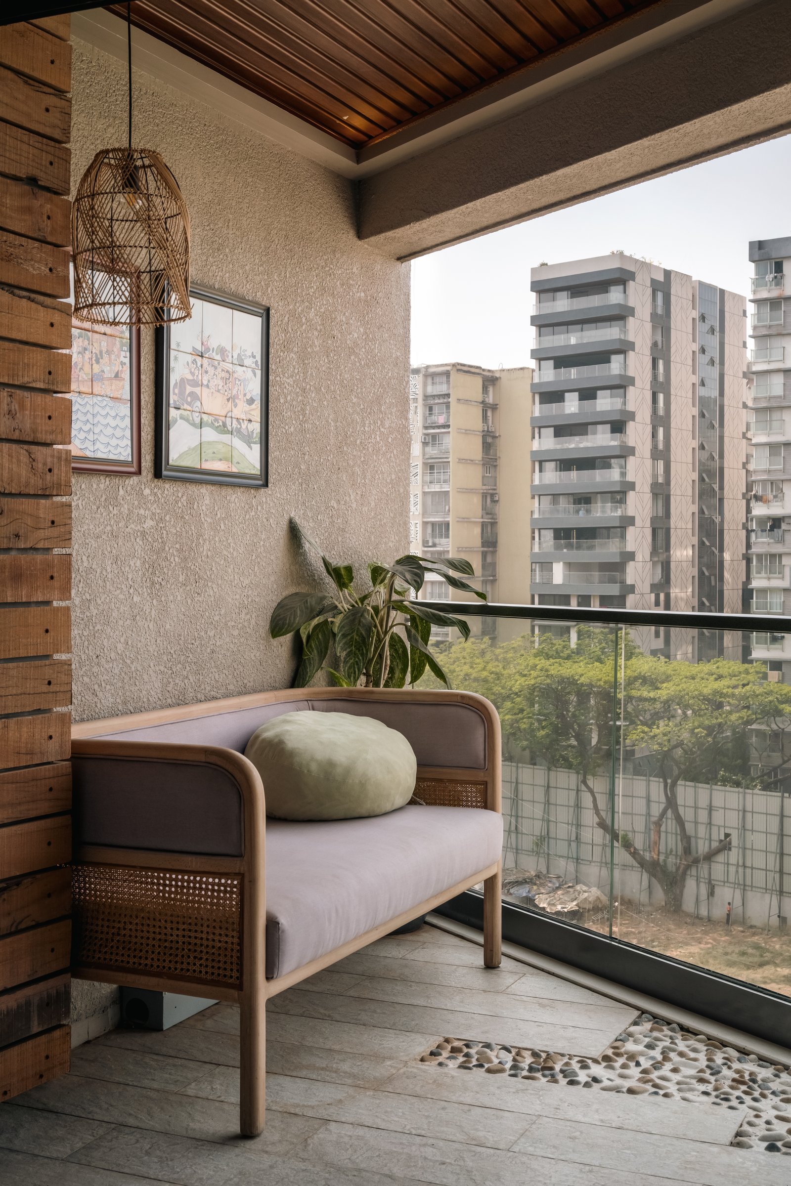 The balcony as a proper room, with a cane-and-wood loveseat, a rattan pendant and a river-pebble inlay in the floor