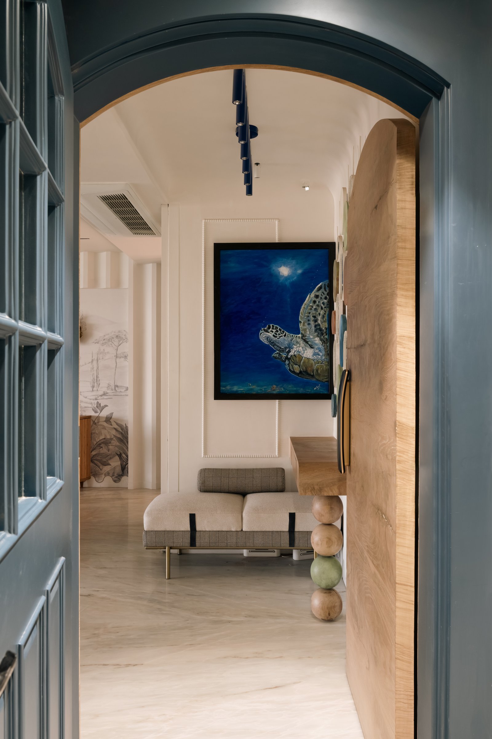The entry, where a deep teal arch frames a marble foyer, a stacked-sphere console and a moody underwater painting