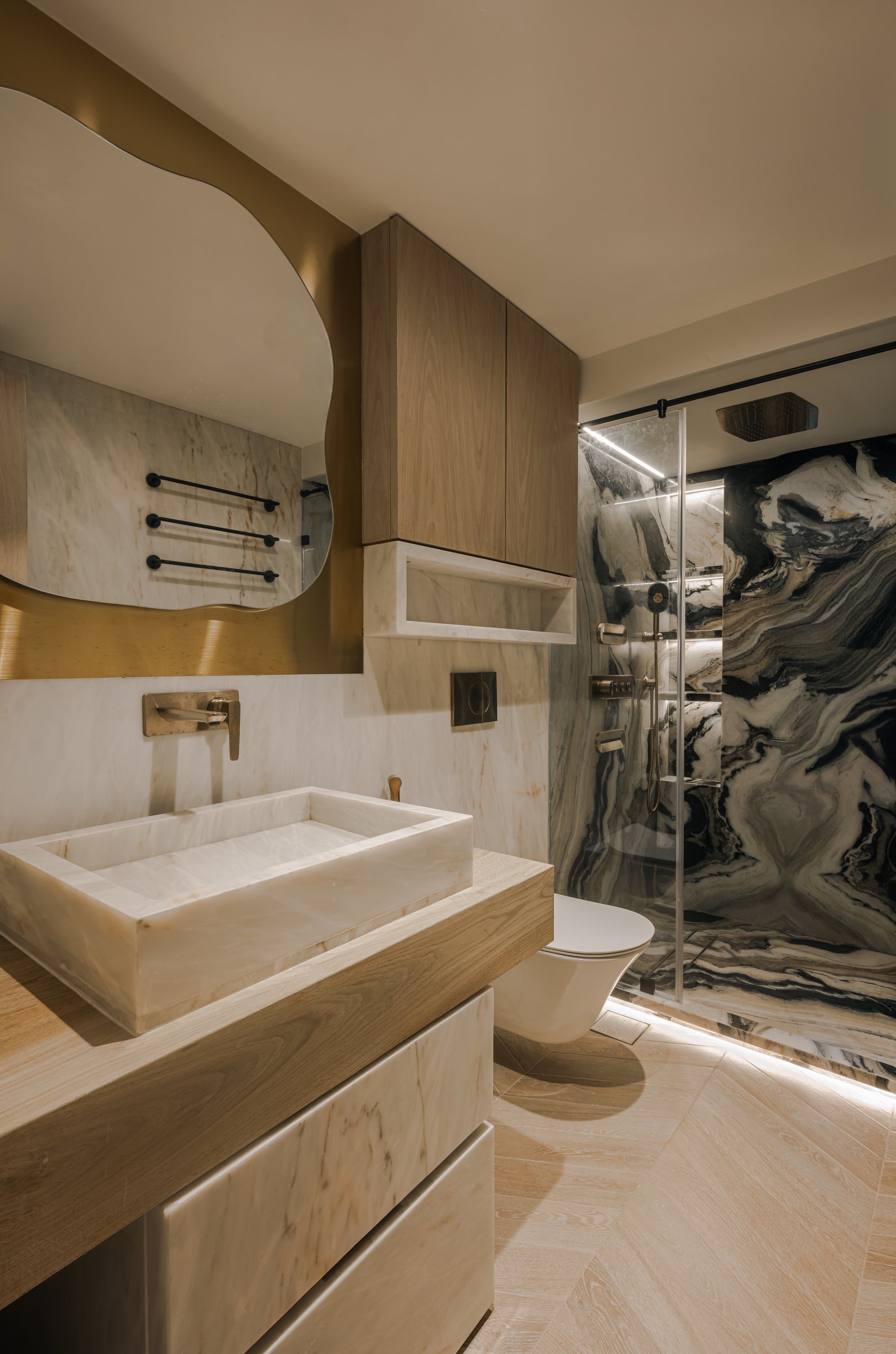 The master bathroom, where a dramatically veined stone slab meets quieter cream marble and warm wood vanity joinery