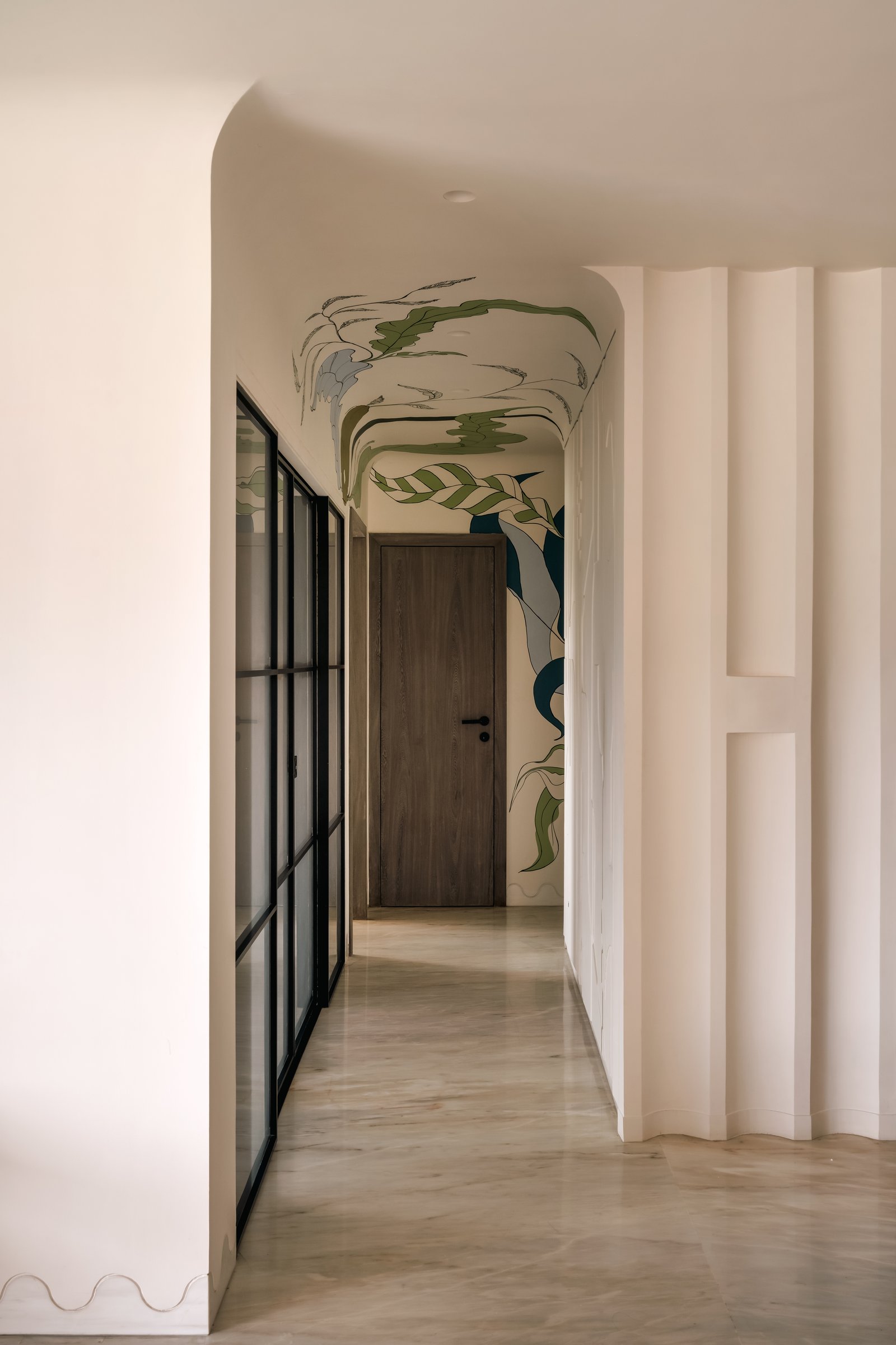 The connecting passage: a curved ceiling carrying a hand-painted botanical mural, with fluted plaster on one side and a steel-and-glass partition on the other