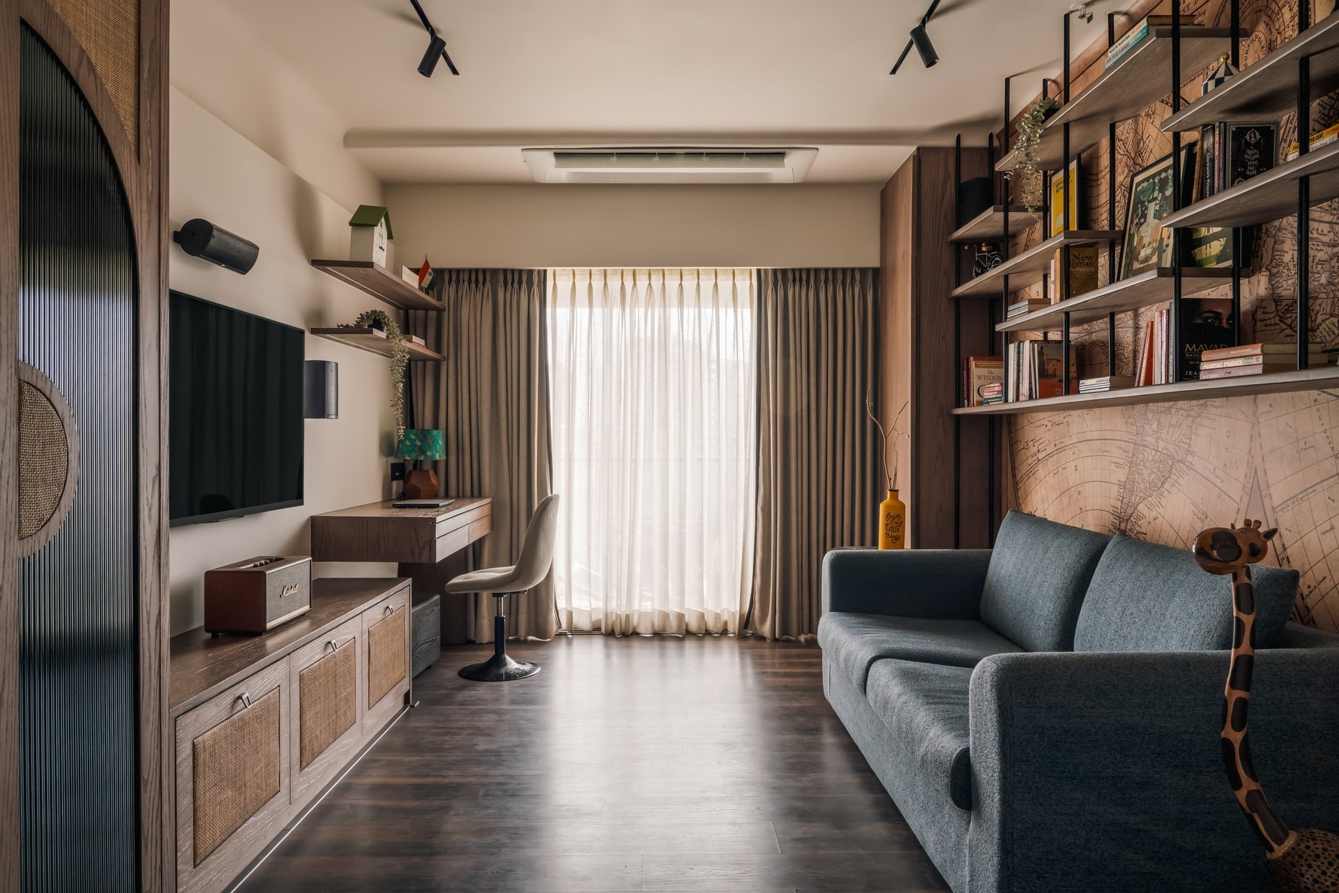 The study, where a wall-mounted television, cane-fronted media unit and slate-blue sofa share space with an open shelving system