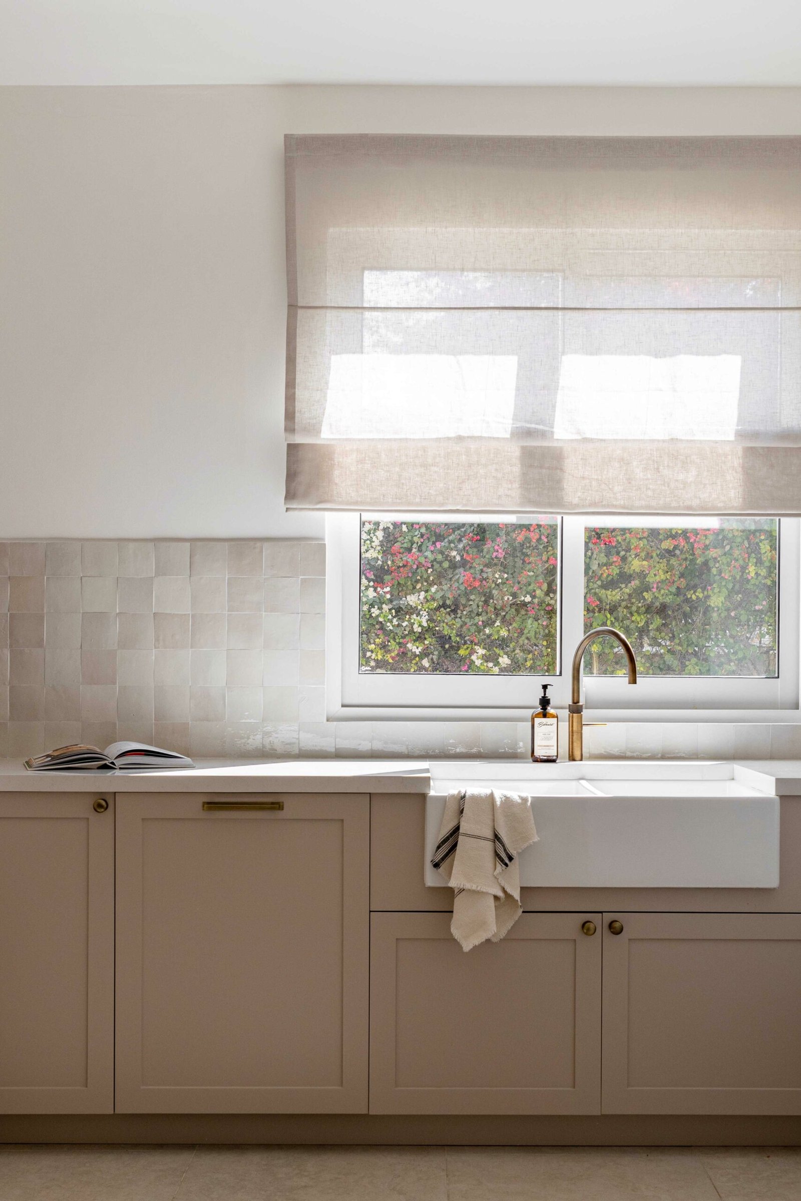 The kitchen, where hand-glazed zellige tile meets putty cabinetry and a farmhouse sink in a tightly held three-note palette